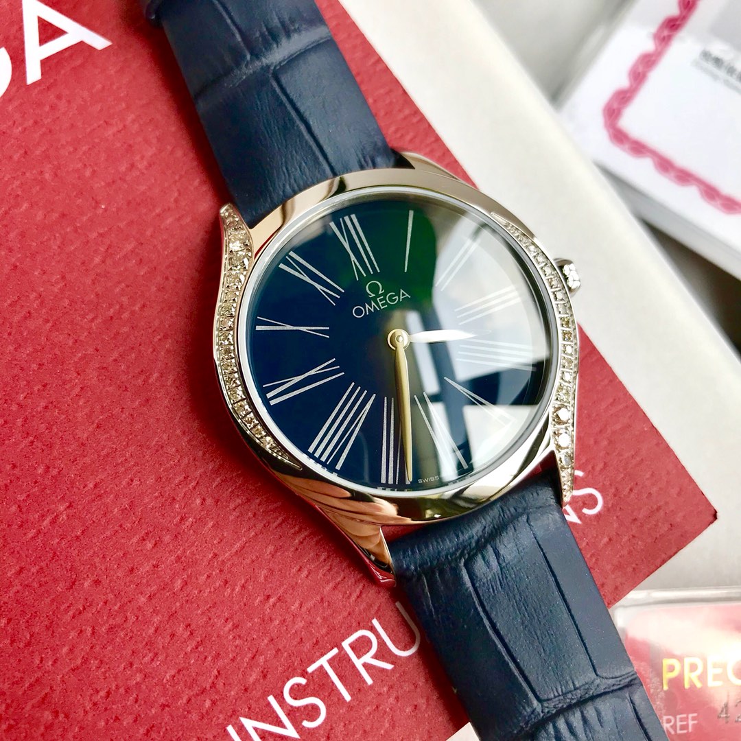 批:2100 新款硬货到！1949年的时候，欧米茄首次使用“Trésor”（法语意思是珍宝）为一个腕表系列命名，成为名典。今年欧米茄推出全新的蝶飞名典系列，配备圆弧形耐磨损蓝宝石玻璃表镜，内部经防反光处理，瑞士石英机芯，牛皮表带，直径36毫米表壳，传承了之前表款纤薄表壳的设计，可以衬托出纤细的手腕，腕表两侧呈现出流畅的曲线，并且还镶嵌有闪耀的钻石，VVS0.9-2.3不同尺寸共计36颗，总重0.693克拉，VVS2.3的钻可以说是迄今为止表壳镶钻尺寸之最了，造价不菲，搭配亮漆表盘，表盘上采用转印独特的罗马数字，指针则经过镀铑处理尽显女性典雅的气质。还有绝美的表冠上花朵图案是由5个欧米茄品牌标识交叠而成，并由红色液态陶瓷打造，尽显鲜活之姿十分别致，重点是花蕊中还镶有一颗璀璨的VVS1.0真钻，将奢华进行到底。配全套包装！送礼体面