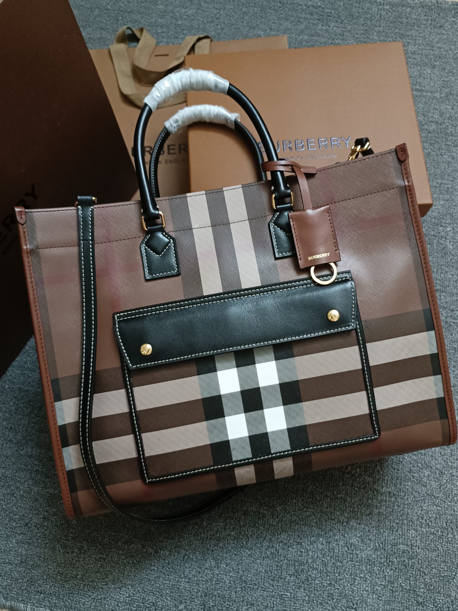 Burberry's latest birch brown plaid tote bag is made of plaid material and topstitched cowhide. Carry it by hand using the top handle or use the