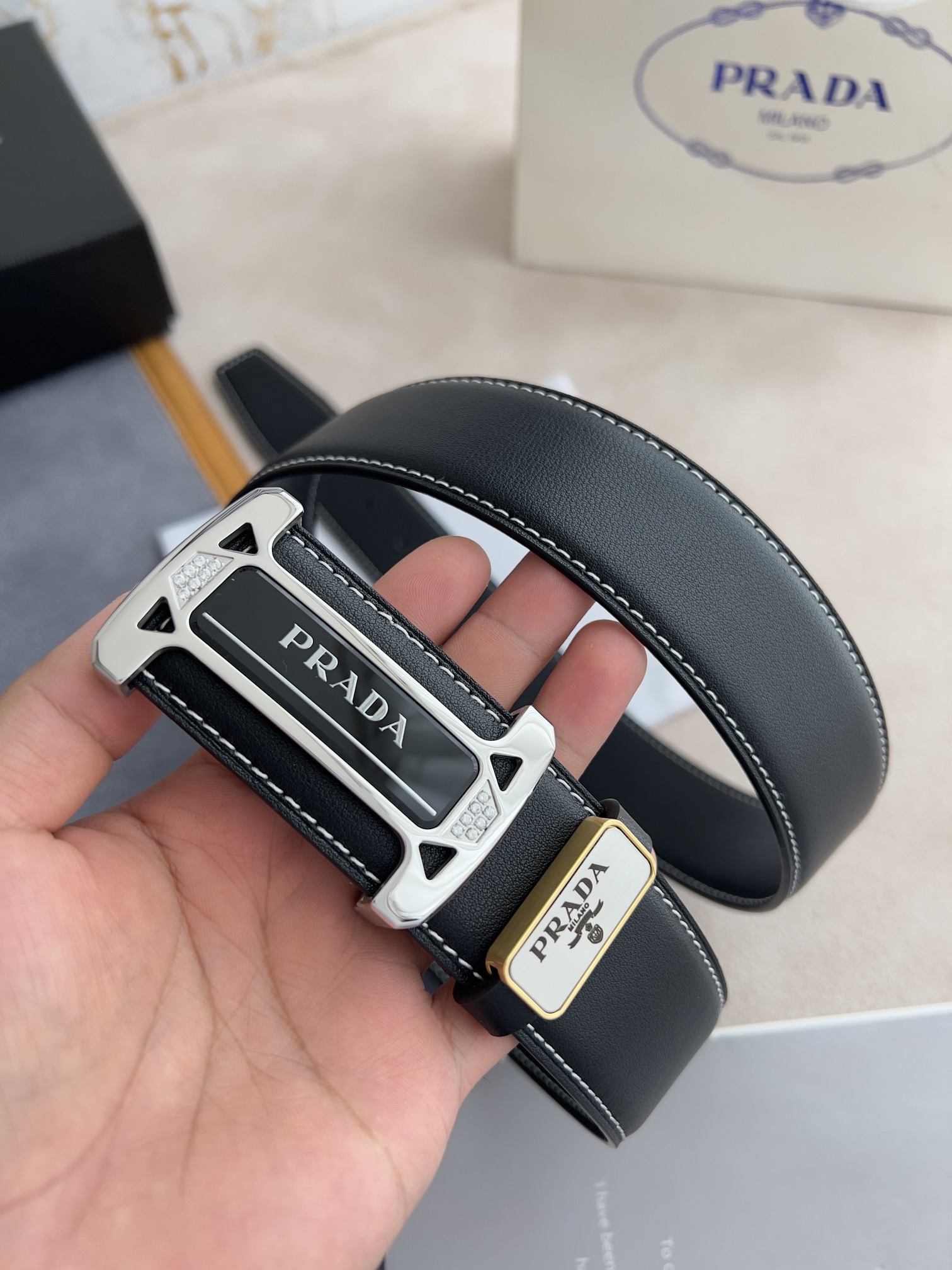 I5  Prada 普拉达  原单腰带·皮带 型号：挂扣,经典亚克力纯钢材质挂扣,镶钻扣,图片实物拍摄 材料：百分百头层牛皮,保证真皮.24k纯钢扣双面可用专柜同等质量, 双面头层牛皮黑色平纹,亚克力贴片扣,镶钻扣,银扣,送人自用首选 包装请认准如图专柜包装,赠送打孔器,原版电子发票,宽度3.8mm