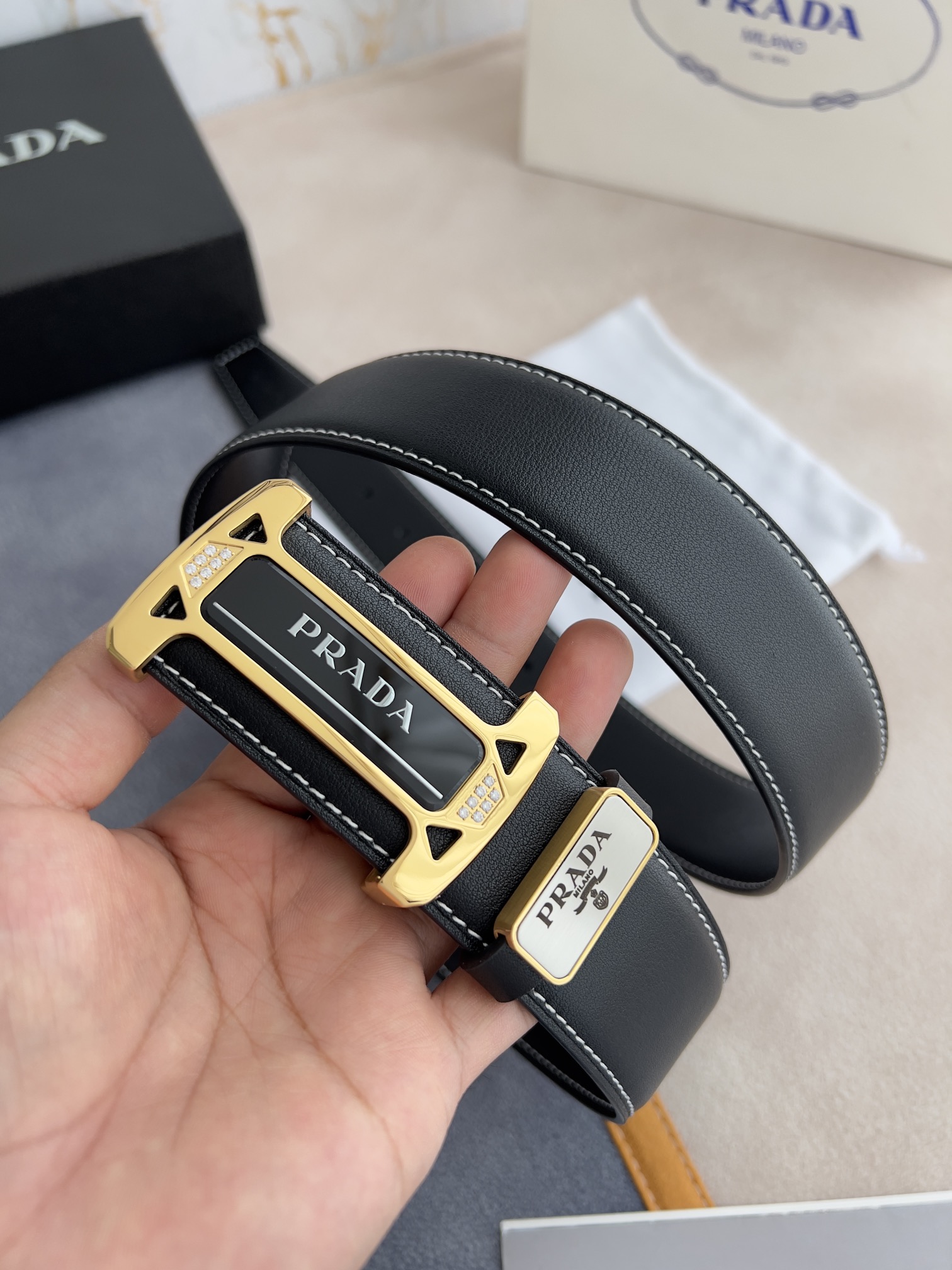 I5  Prada 普拉达  原单腰带·皮带 型号：挂扣,经典亚克力纯钢材质挂扣,镶钻扣,图片实物拍摄 材料：百分百头层牛皮,保证真皮.24k纯钢扣双面可用专柜同等质量, 双面头层牛皮黑色平纹,亚克力贴片扣,镶钻扣,金扣,送人自用首选 包装请认准如图专柜包装,赠送打孔器,原版电子发票,宽度3.8mm