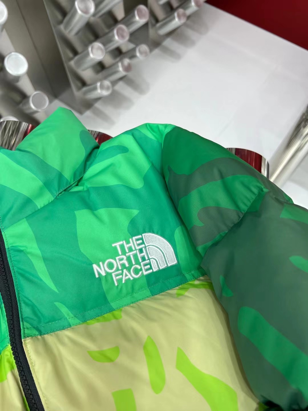 North Face x KAWS 1996 Nuptse collaboration in green and gray. Sizes XS-XXL. Bold design with vibrant colors and KAWS graphics.-Big cat
