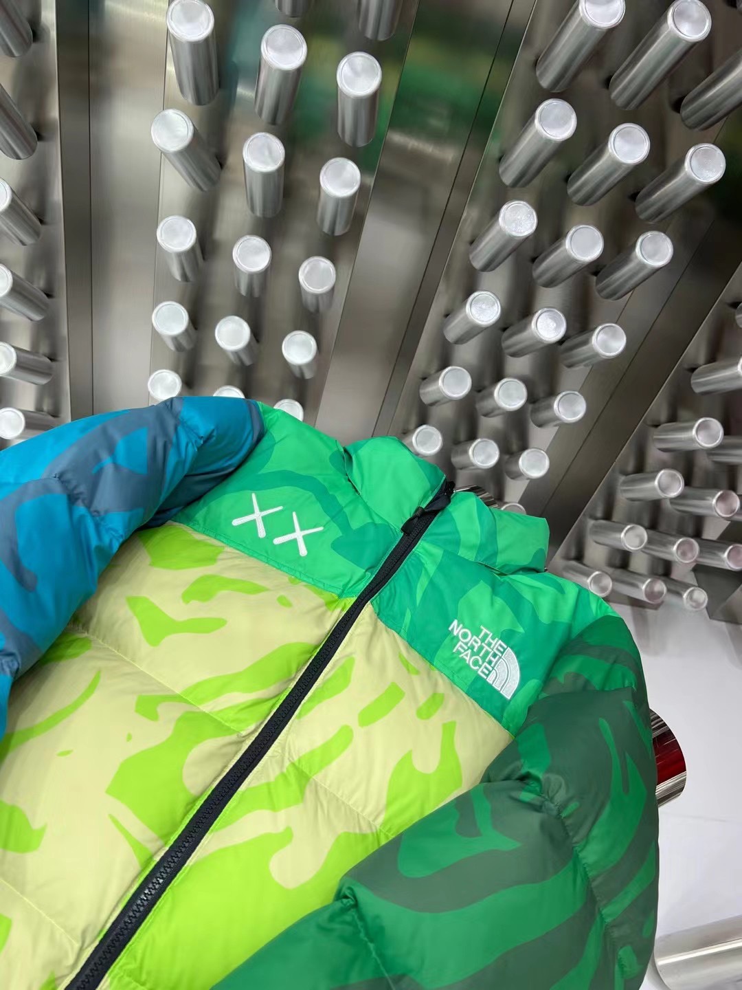 North Face x KAWS 1996 Nuptse collaboration in green and gray. Sizes XS-XXL. Bold design with vibrant colors and KAWS graphics.-Big cat