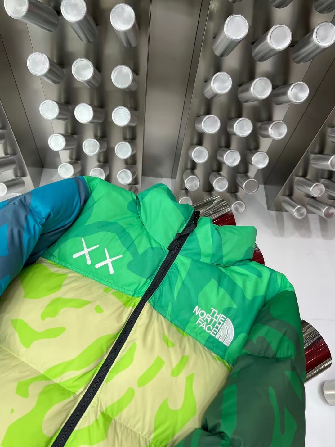 North Face x KAWS 1996 Nuptse collaboration in green and gray. Sizes XS-XXL. Bold design with vibrant colors and KAWS graphics.-Big cat