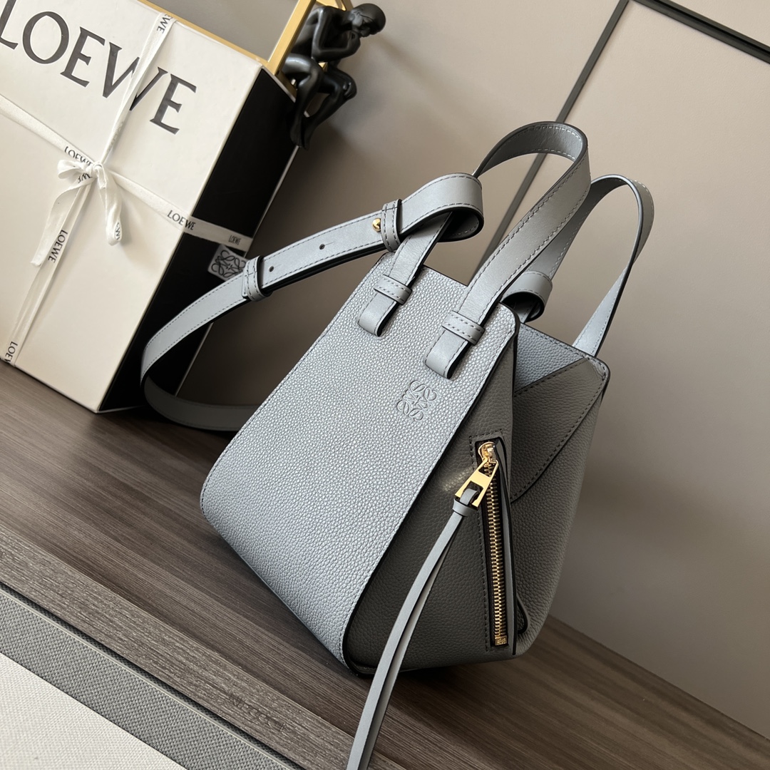 Loewe Soft Grained Calfskin Compact Hammock Handbag (New Size) New Version 🆕 The Hammock bag is a versatile handbag with soft side panels that can be released to change its shape. This new compact version is made of soft grained calfskin leather. It can be worn as a shoulder bag, crossbody, handheld, or carried by the top handle. Features detachable and adjustable shoulder strap, interior hook closure, two interior pockets, customizable with shoulder strap and personalized charms, an external zip pocket, and lined with Anagram cotton canvas. Size: 20*19*14 cm. Model: 65223595. image 1