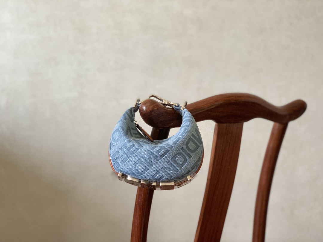 Fendi Mini Nano Crescent bag in light blue denim with FENDI Mirror pattern all over and brown leather details. When the handbag is carried under