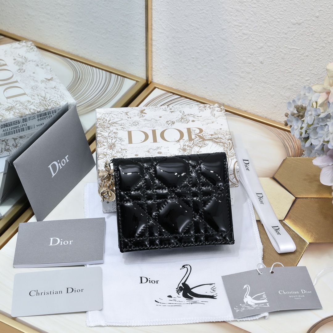 Dior 这款翻盖卡夹采用黑色漆皮牛皮革精心制作，彰显Lady r 系列 设计，搭配藤格纹缉面线和D.I.O.R.吊饰
