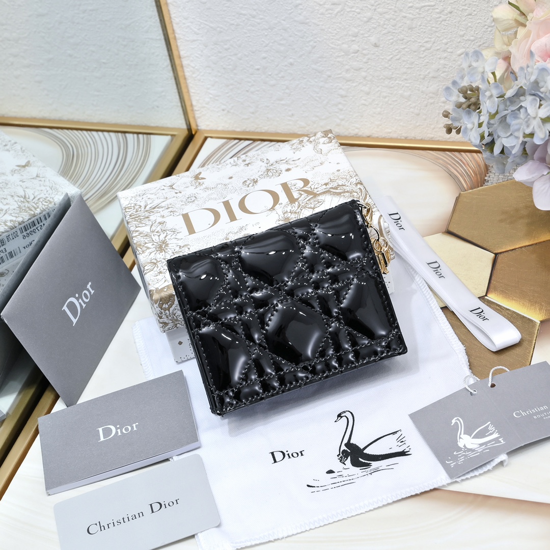 Dior 这款翻盖卡夹采用黑色漆皮牛皮革精心制作，彰显Lady r 系列 设计，搭配藤格纹缉面线和D.I.O.R.吊饰
