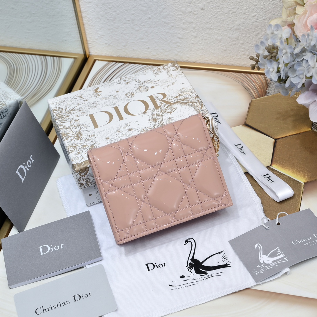 Dior 这款翻盖卡夹采用黑色漆皮牛皮革精心制作，彰显Lady r 系列 设计，搭配藤格纹缉面线和D.I.O.R.吊饰