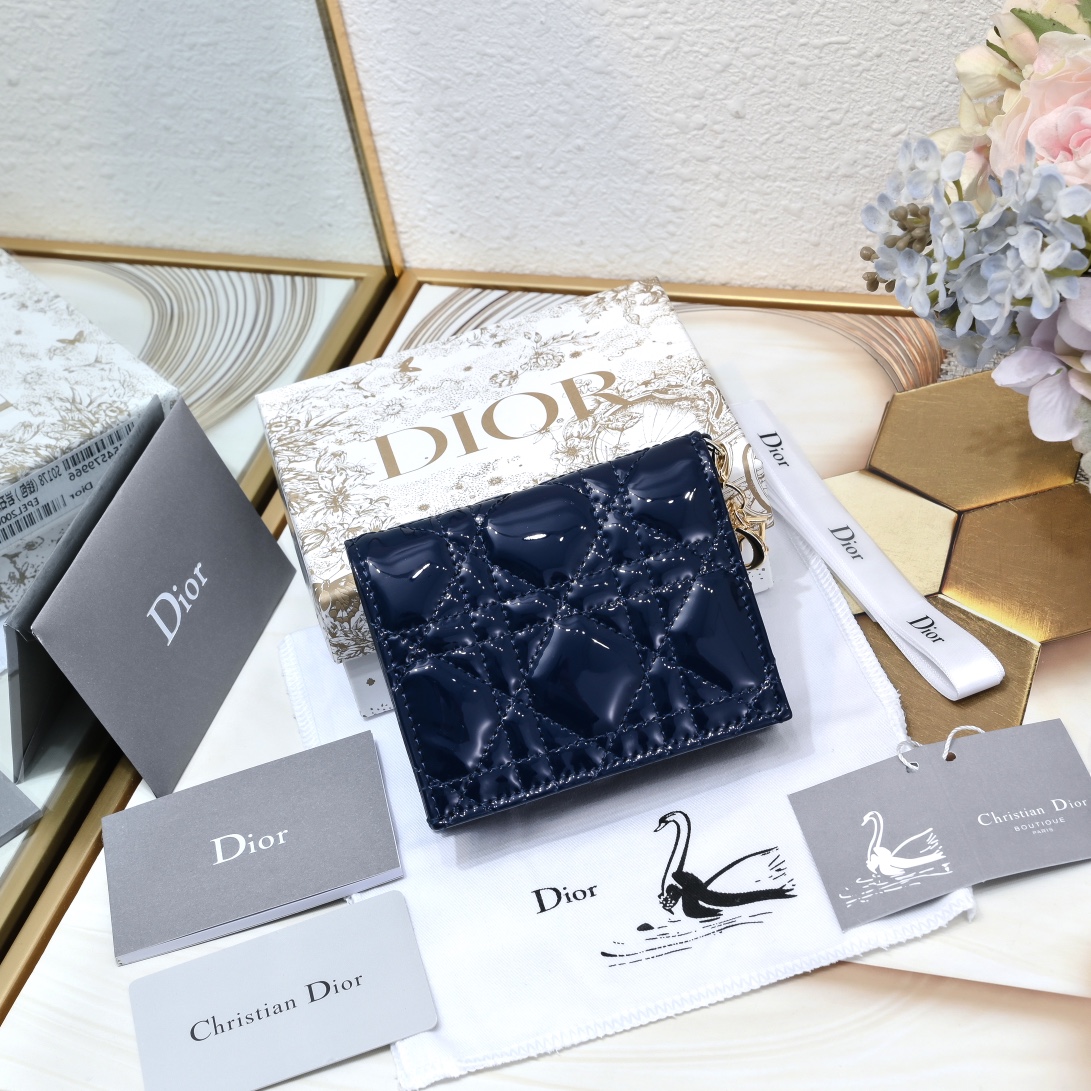 Dior 这款翻盖卡夹采用黑色漆皮牛皮革精心制作，彰显Lady r 系列 设计，搭配藤格纹缉面线和D.I.O.R.吊饰