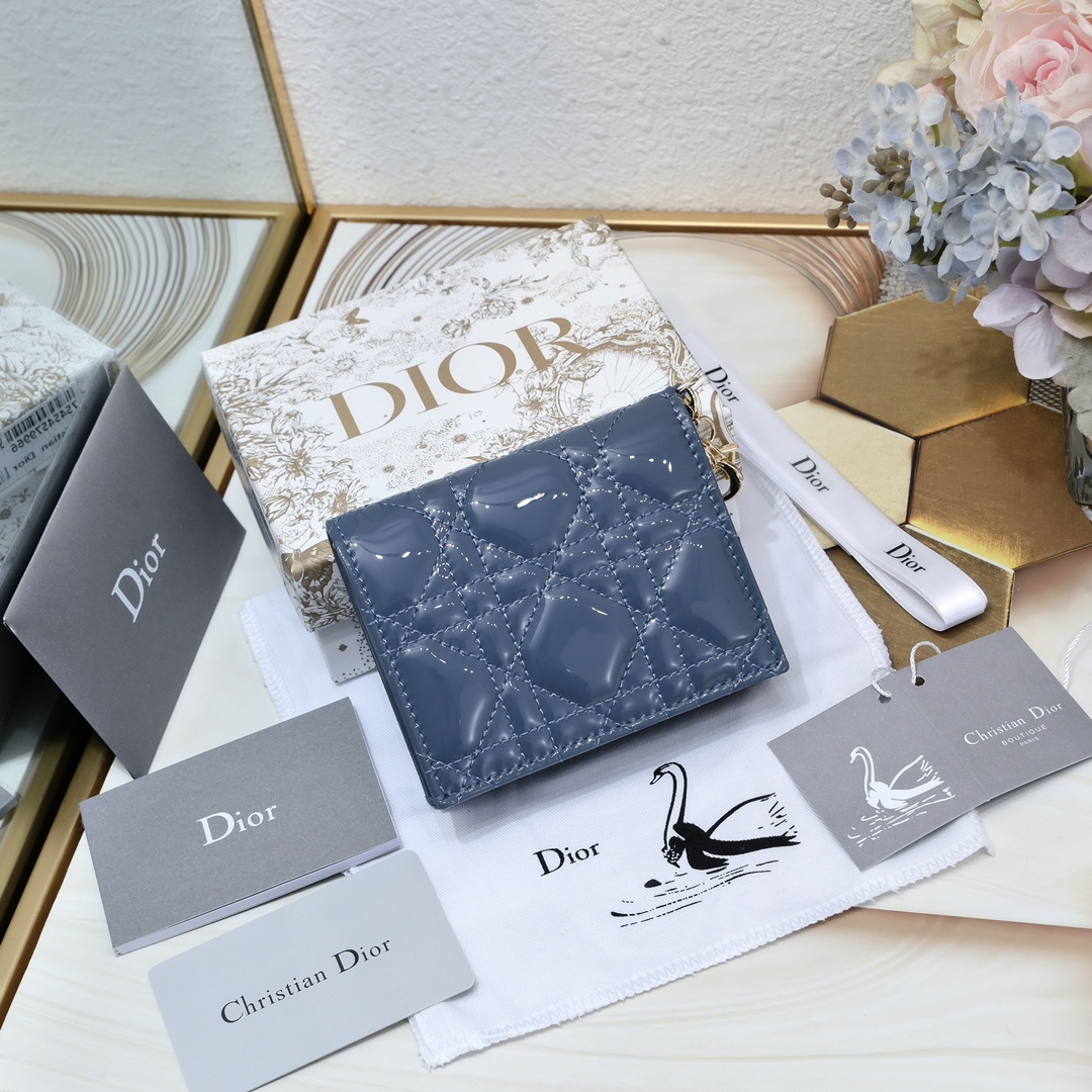 Dior 这款翻盖卡夹采用黑色漆皮牛皮革精心制作，彰显Lady r 系列 设计，搭配藤格纹缉面线和D.I.O.R.吊饰