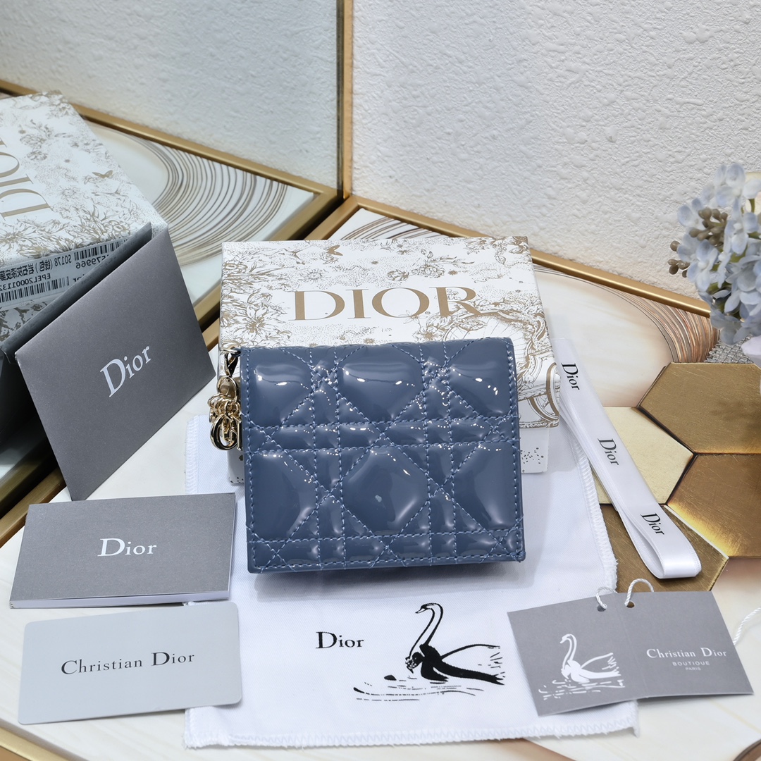 Dior 这款翻盖卡夹采用黑色漆皮牛皮革精心制作，彰显Lady r 系列 设计，搭配藤格纹缉面线和D.I.O.R.吊饰