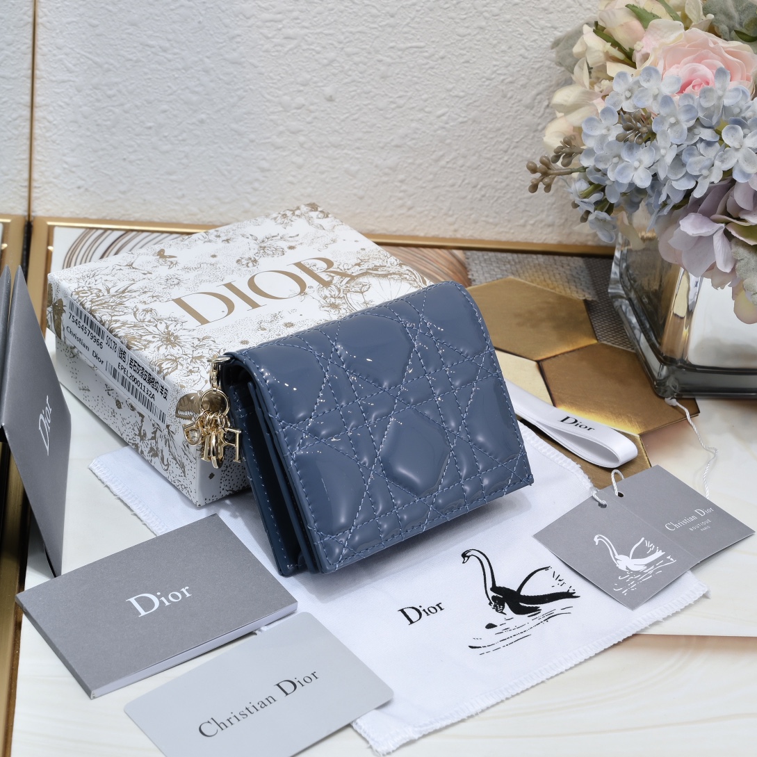 Dior 这款翻盖卡夹采用黑色漆皮牛皮革精心制作，彰显Lady r 系列 设计，搭配藤格纹缉面线和D.I.O.R.吊饰