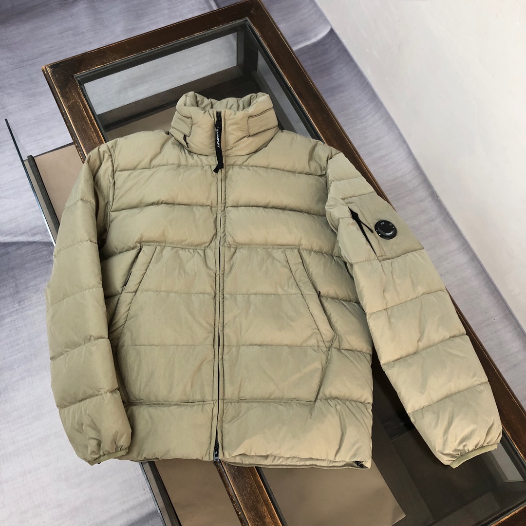p565.00 CP.COMPANY 新款专柜同步，CP经典羽绒服，90进口羽绒 特殊高密记忆面料原厂染色防水，具备透气且防风功能 上身体感保温舒适度极好  简洁大方的设计 深受户外旅游爱好人士偏爱 也适合平时商务穿着的百搭款 所有辅料原版定制 实物拍照 现货供应  
颜色：黑色 卡其色 橘色
尺码：M-L-XL-XXL

