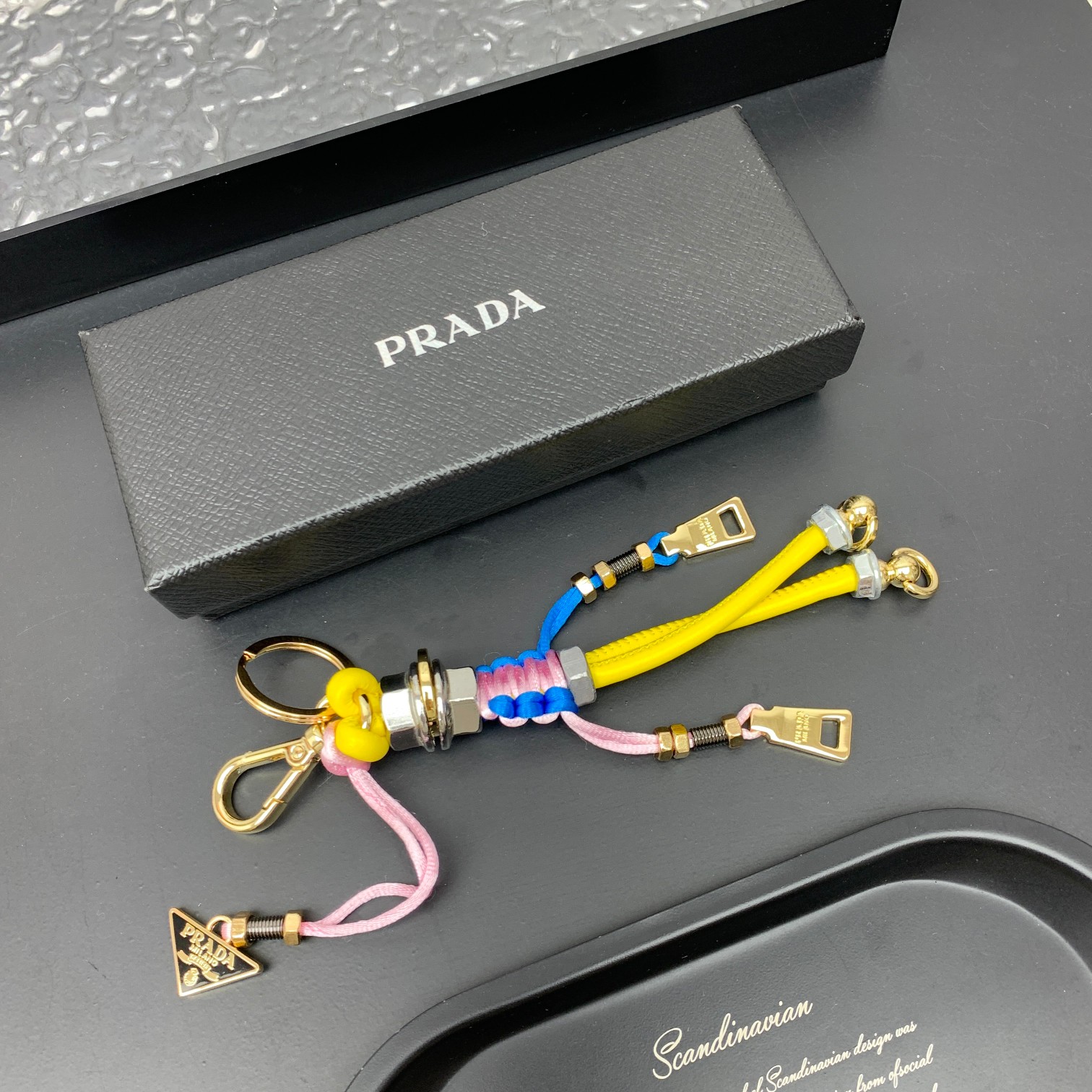 新款🌟这款钥匙扣呈现 Saffiano 牛皮革手工编织富有辨识度的十字纹理，饰有标志性的涂珐琅金属徽标。