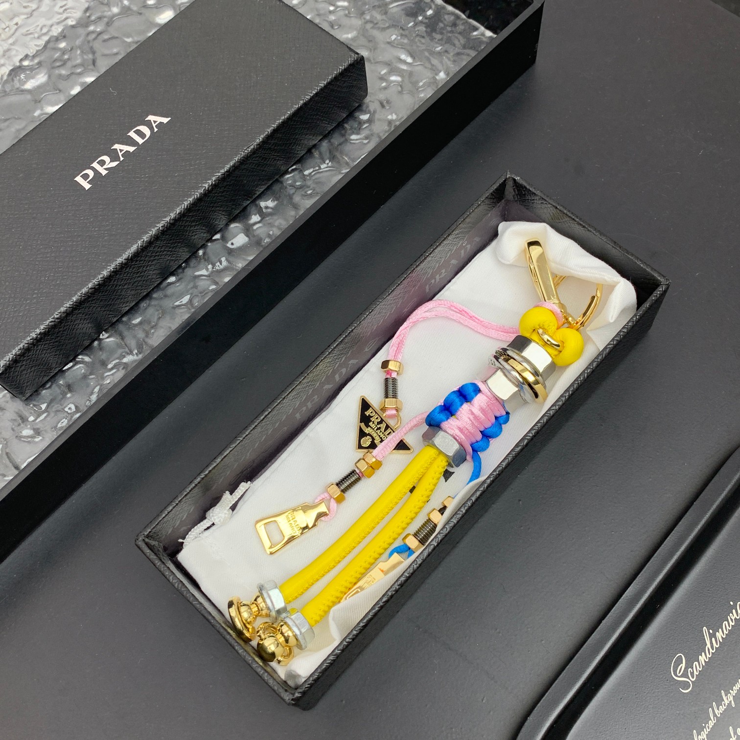 新款🌟这款钥匙扣呈现 Saffiano 牛皮革手工编织富有辨识度的十字纹理，饰有标志性的涂珐琅金属徽标。