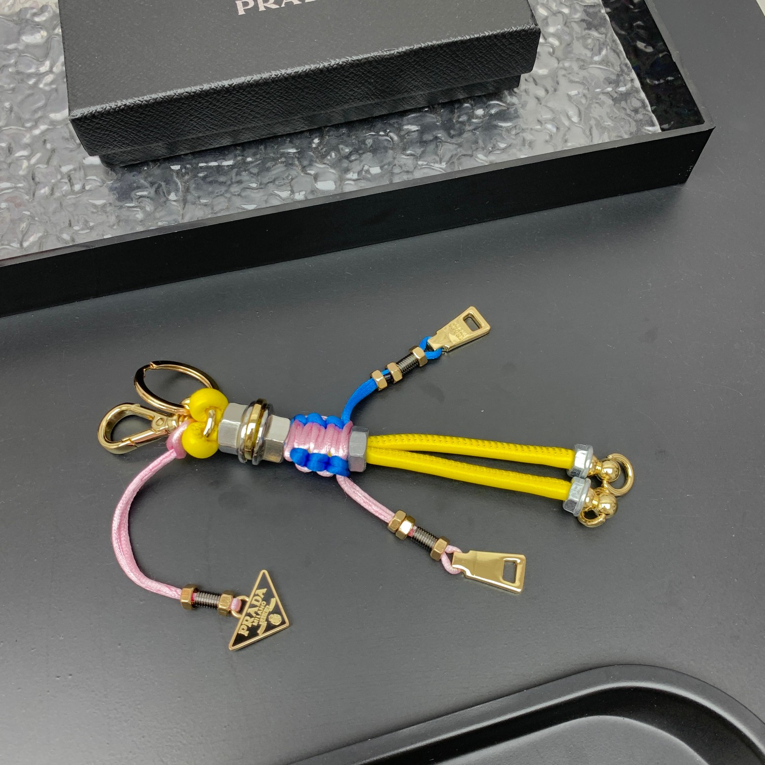 新款🌟这款钥匙扣呈现 Saffiano 牛皮革手工编织富有辨识度的十字纹理，饰有标志性的涂珐琅金属徽标。
