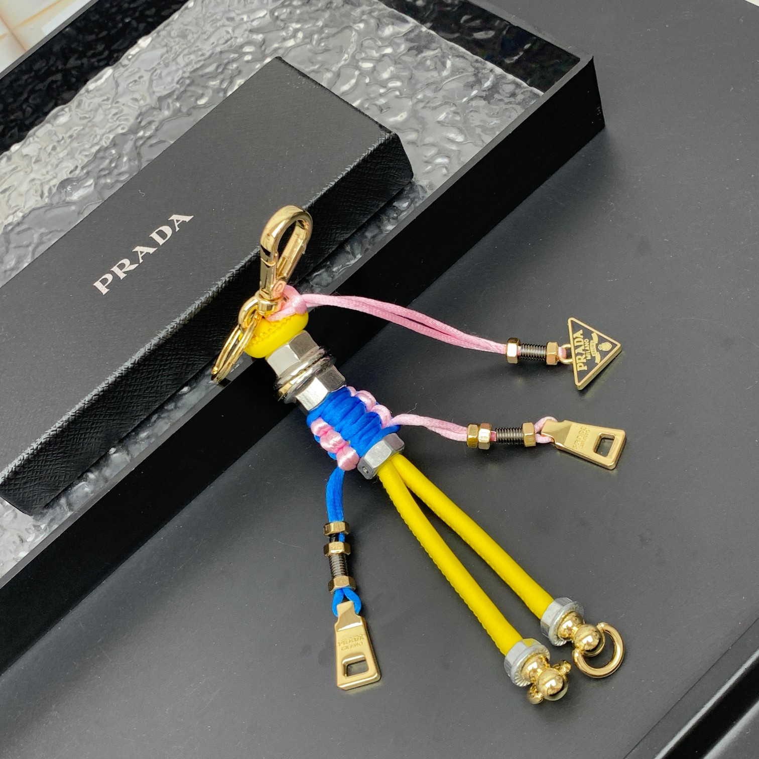 新款🌟这款钥匙扣呈现 Saffiano 牛皮革手工编织富有辨识度的十字纹理，饰有标志性的涂珐琅金属徽标。