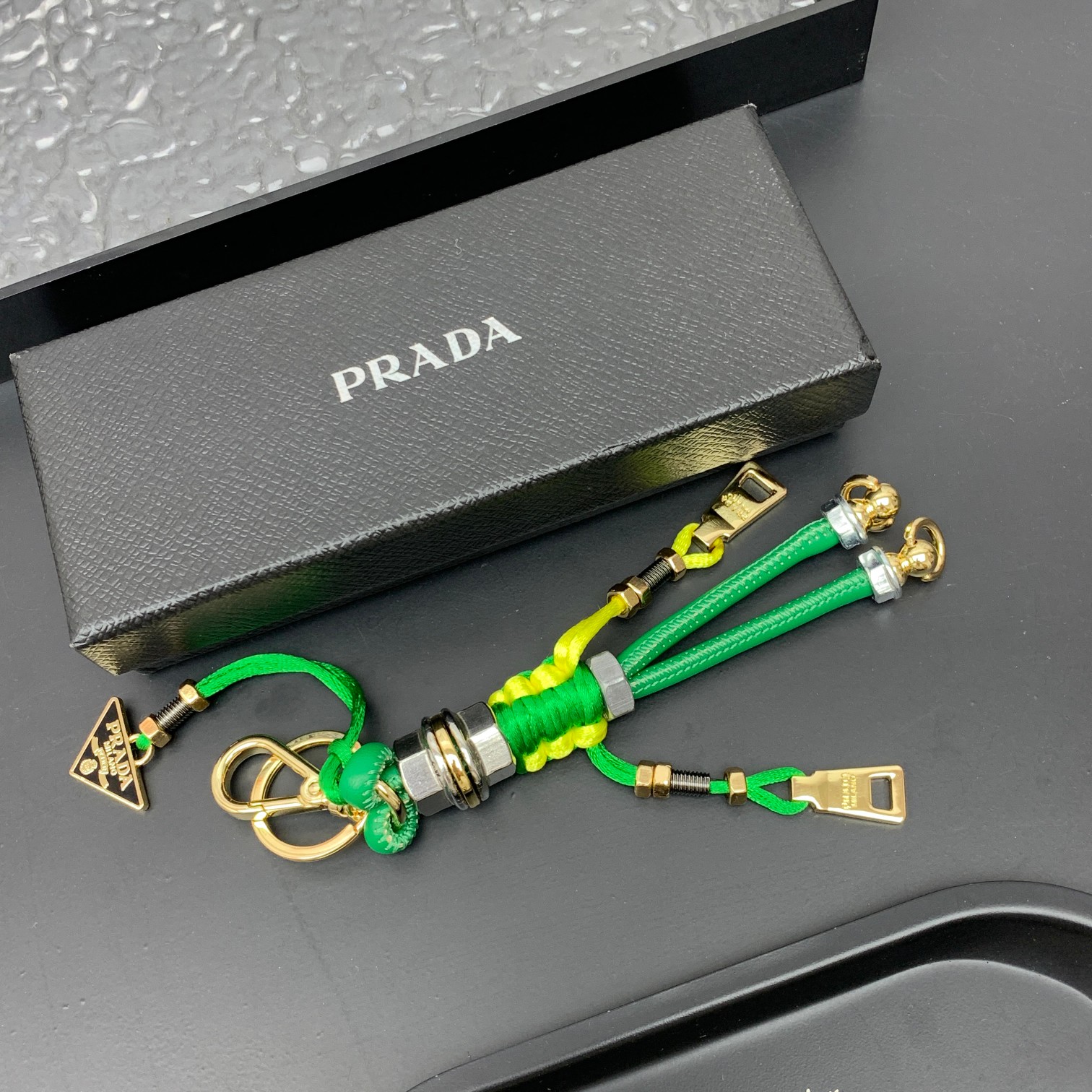 新款🌟这款钥匙扣呈现 Saffiano 牛皮革手工编织富有辨识度的十字纹理，饰有标志性的涂珐琅金属徽标。