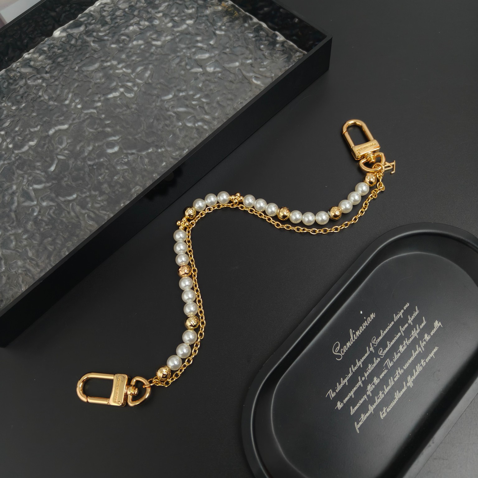 LV 腰带链以双链设计宣示潮流个性：一条融汇珠饰，并以金属串珠拼写 VUITTON 标识，另一条借链环释