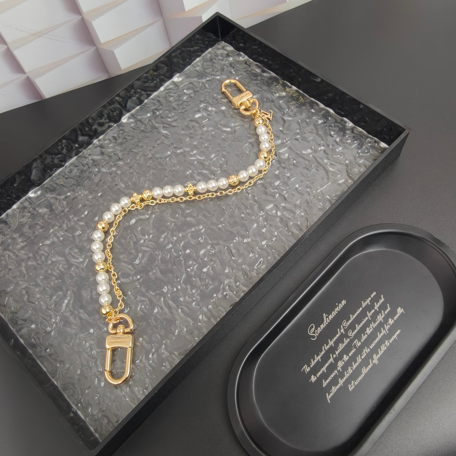 LV 腰带链以双链设计宣示潮流个性：一条融汇珠饰，并以金属串珠拼写 VUITTON 标识，另一条借链环释