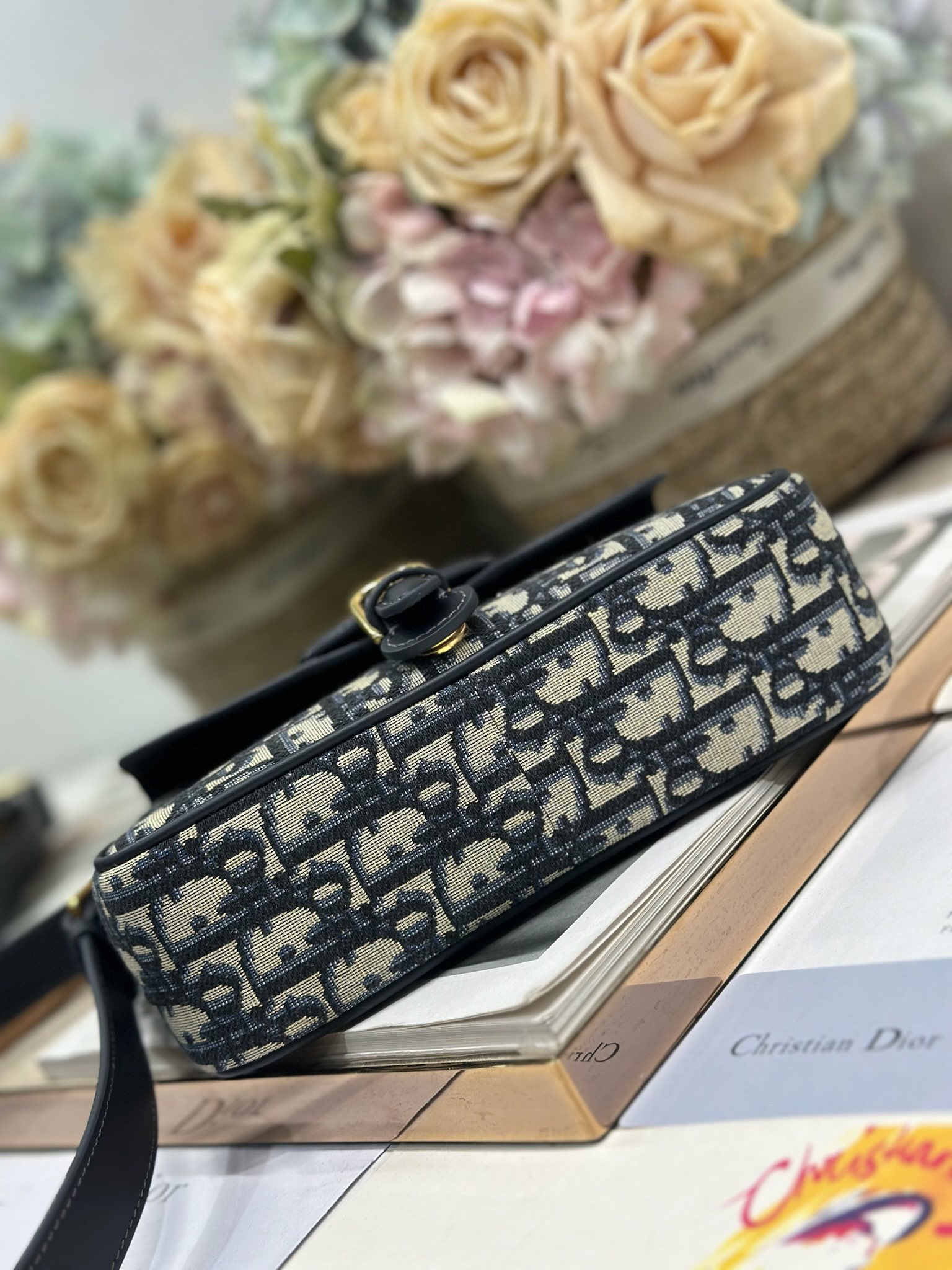 Dior 新款波比拉链小包 「蓝D布配皮」
这款波比拉链手袋是二零二五春夏成衣系列新品，采用蓝色 Oblique 印花面料等材质精心制作，优雅实用的设计提升该系列的格调。同色调光滑牛皮革翻盖饰以复古金色饰面金属细节，饰以拉链开口，配可调节肩带，手提、肩背或斜挎。p560

翻盖开合
拉链开口
可调节、可拆卸的皮革带
内部插袋

型号：2358
尺寸：20 X13.5 X5.5 厘米（长 x 高 x 宽）