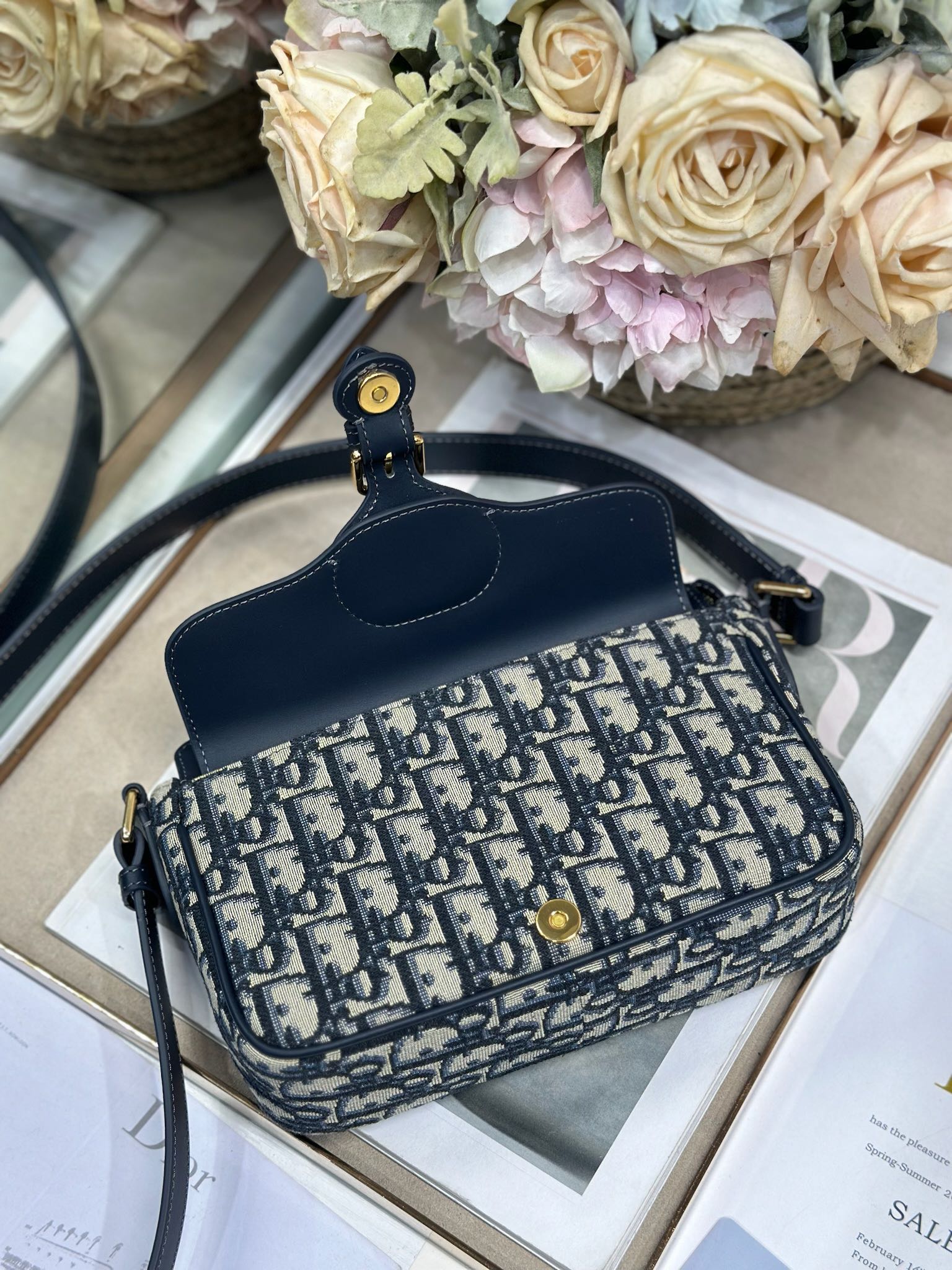 Dior 新款波比拉链小包 「蓝D布配皮」
这款波比拉链手袋是二零二五春夏成衣系列新品，采用蓝色 Oblique 印花面料等材质精心制作，优雅实用的设计提升该系列的格调。同色调光滑牛皮革翻盖饰以复古金色饰面金属细节，饰以拉链开口，配可调节肩带，手提、肩背或斜挎。p560

翻盖开合
拉链开口
可调节、可拆卸的皮革带
内部插袋

型号：2358
尺寸：20 X13.5 X5.5 厘米（长 x 高 x 宽）