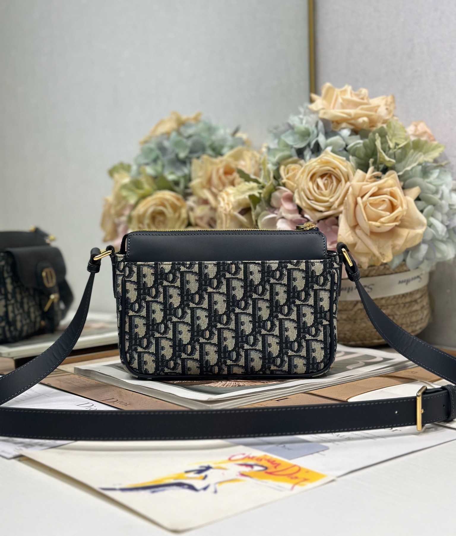 Dior 新款波比拉链小包 「蓝D布配皮」
这款波比拉链手袋是二零二五春夏成衣系列新品，采用蓝色 Oblique 印花面料等材质精心制作，优雅实用的设计提升该系列的格调。同色调光滑牛皮革翻盖饰以复古金色饰面金属细节，饰以拉链开口，配可调节肩带，手提、肩背或斜挎。p560

翻盖开合
拉链开口
可调节、可拆卸的皮革带
内部插袋

型号：2358
尺寸：20 X13.5 X5.5 厘米（长 x 高 x 宽）