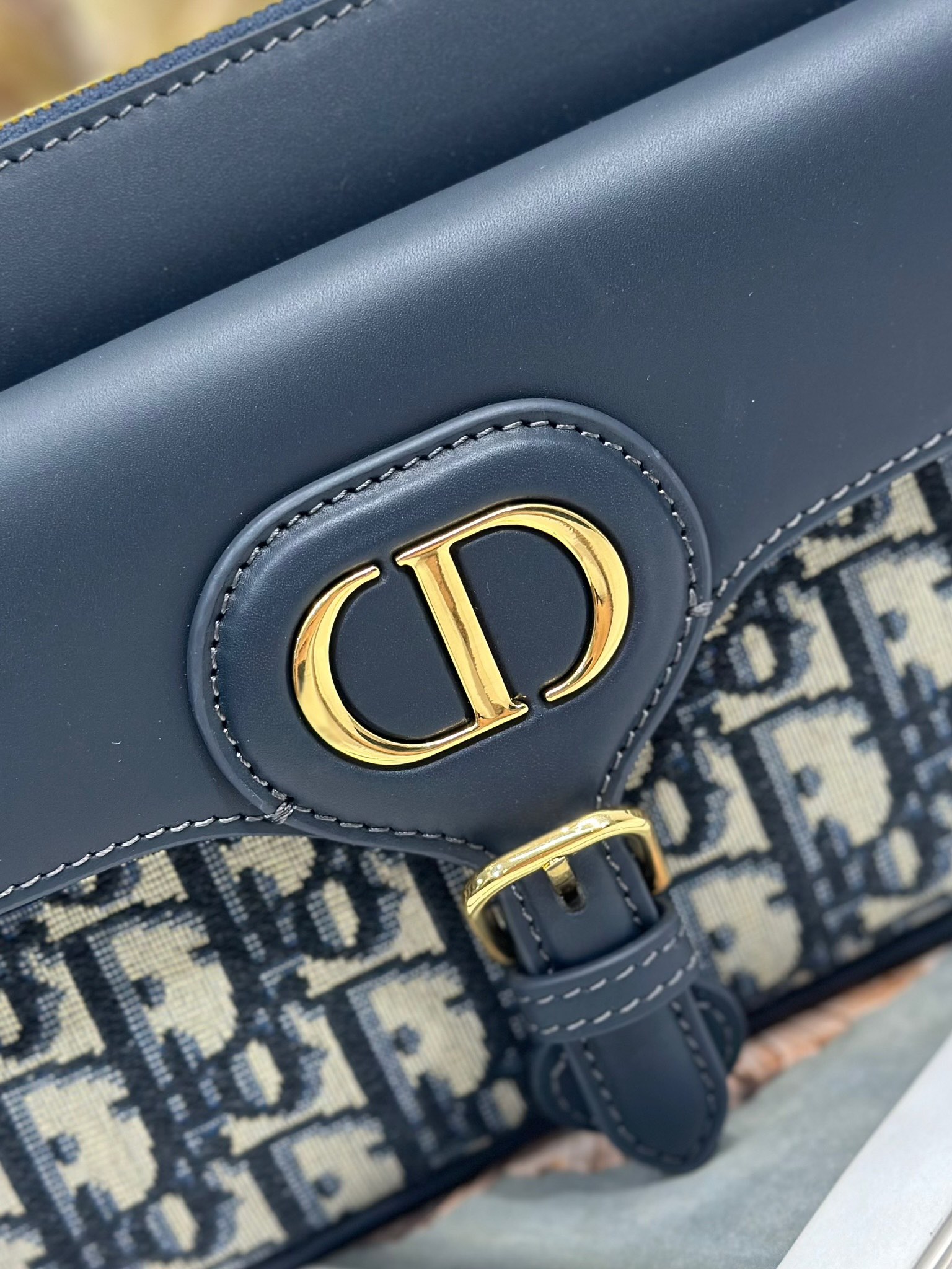 Dior 新款波比拉链小包 「蓝D布配皮」
这款波比拉链手袋是二零二五春夏成衣系列新品，采用蓝色 Oblique 印花面料等材质精心制作，优雅实用的设计提升该系列的格调。同色调光滑牛皮革翻盖饰以复古金色饰面金属细节，饰以拉链开口，配可调节肩带，手提、肩背或斜挎。p560

翻盖开合
拉链开口
可调节、可拆卸的皮革带
内部插袋

型号：2358
尺寸：20 X13.5 X5.5 厘米（长 x 高 x 宽）