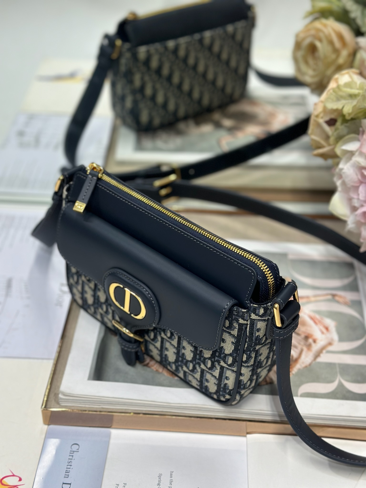 Dior 新款波比拉链小包 「蓝D布配皮」
这款波比拉链手袋是二零二五春夏成衣系列新品，采用蓝色 Oblique 印花面料等材质精心制作，优雅实用的设计提升该系列的格调。同色调光滑牛皮革翻盖饰以复古金色饰面金属细节，饰以拉链开口，配可调节肩带，手提、肩背或斜挎。p560

翻盖开合
拉链开口
可调节、可拆卸的皮革带
内部插袋

型号：2358
尺寸：20 X13.5 X5.5 厘米（长 x 高 x 宽）