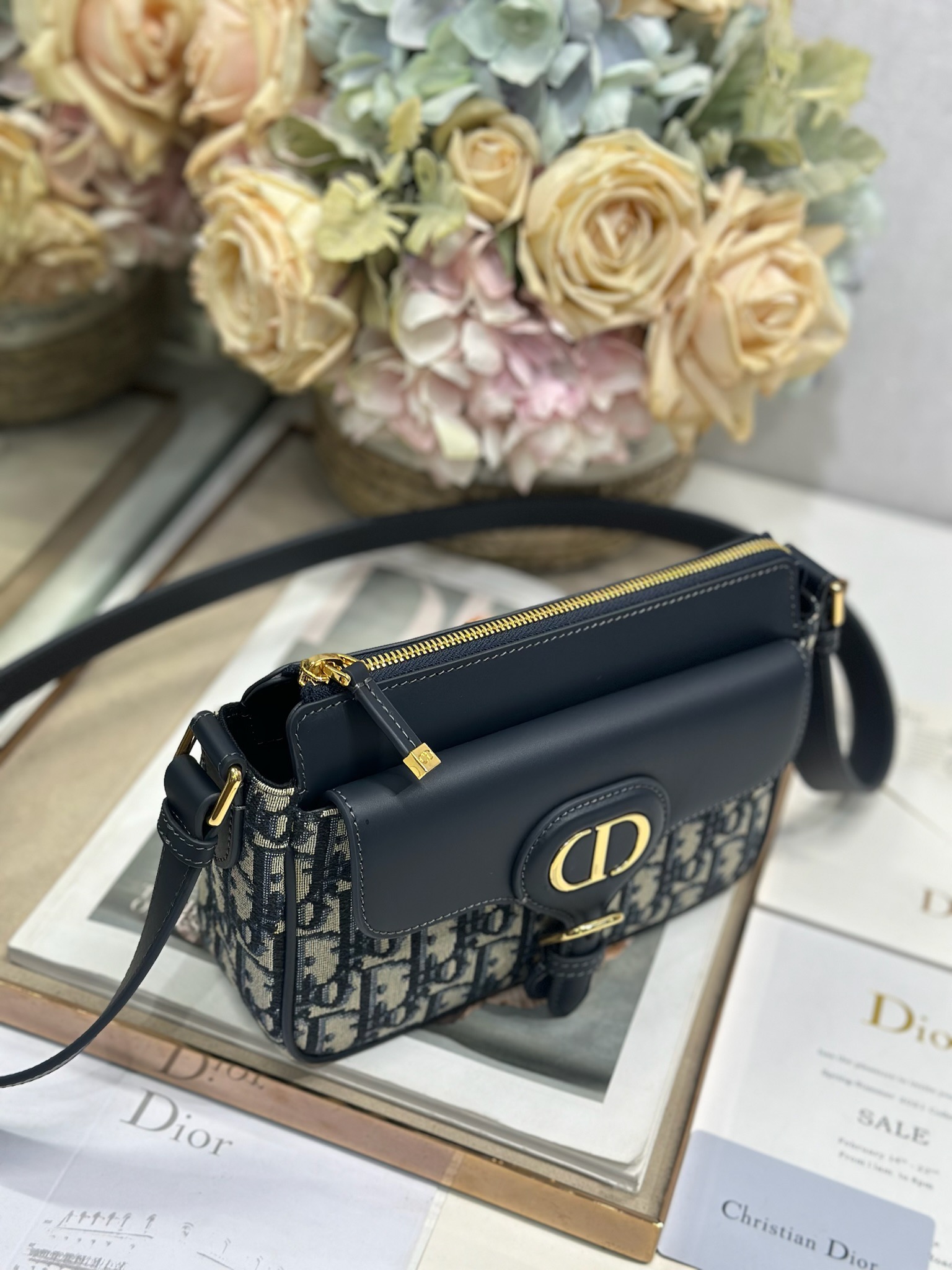 Dior 新款波比拉链小包 「蓝D布配皮」
这款波比拉链手袋是二零二五春夏成衣系列新品，采用蓝色 Oblique 印花面料等材质精心制作，优雅实用的设计提升该系列的格调。同色调光滑牛皮革翻盖饰以复古金色饰面金属细节，饰以拉链开口，配可调节肩带，手提、肩背或斜挎。p560

翻盖开合
拉链开口
可调节、可拆卸的皮革带
内部插袋

型号：2358
尺寸：20 X13.5 X5.5 厘米（长 x 高 x 宽）