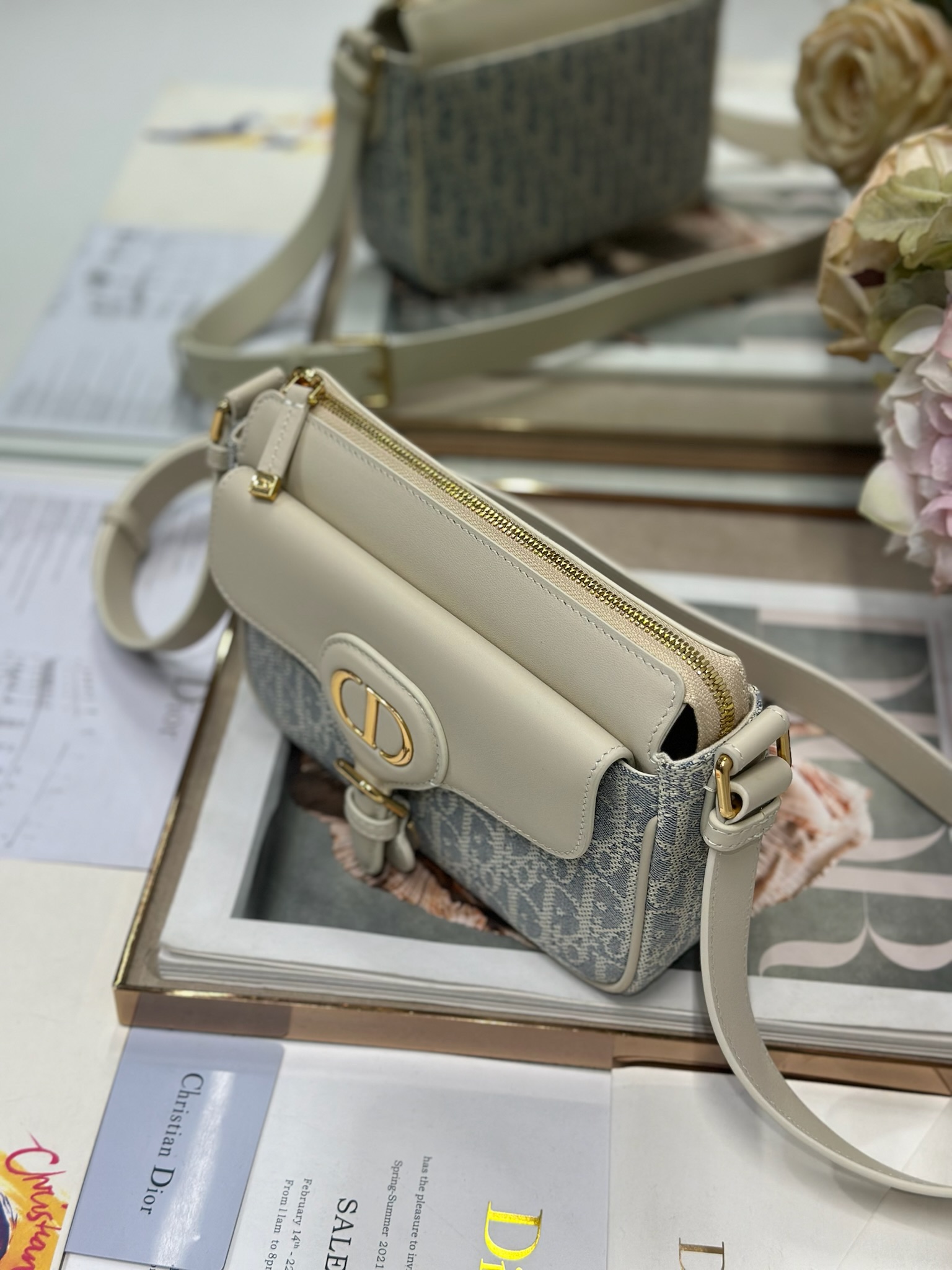 Dior 新款波比拉链小包 「椰子蓝D布配皮」
这款波比拉链手袋是二零二五春夏成衣系列新品，采用椰子蓝 Oblique 印花面料等材质精心制作，优雅实用的设计提升该系列的格调。浅饼干色调光滑牛皮革翻盖饰以复古金色饰面金属细节，饰以拉链开口，配可调节肩带，手提、肩背或斜挎。p560

翻盖开合
拉链开口
可调节、可拆卸的皮革带
内部插袋

型号：2358
尺寸：20 X13.5 X5.5 厘米（长 x 高 x 宽）