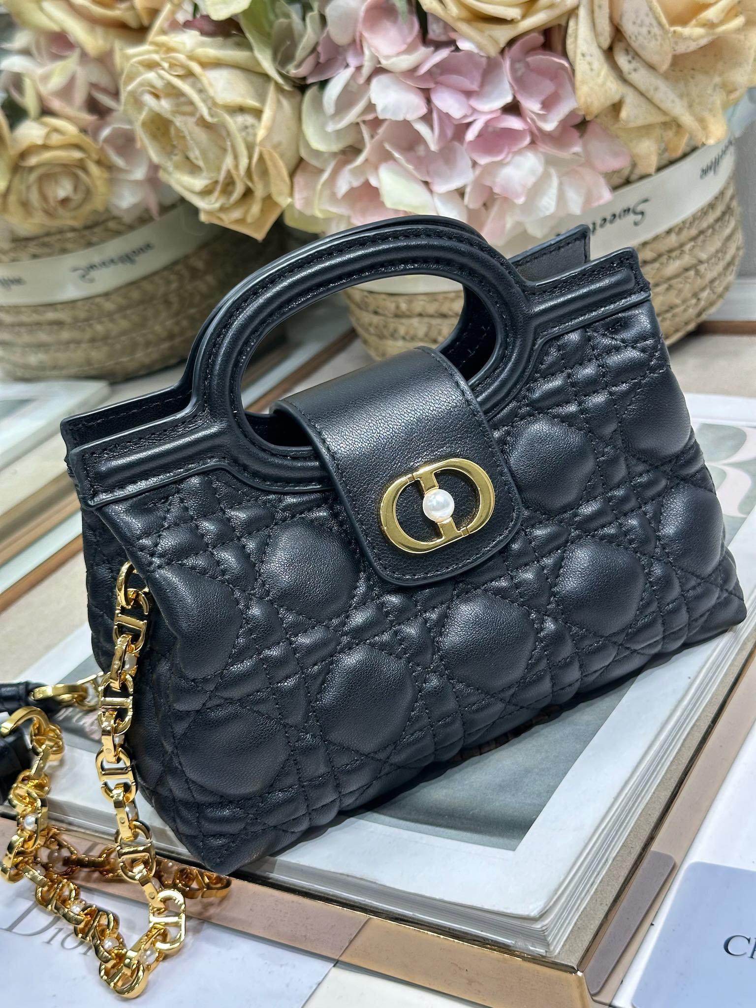 Dior Jolie Top Handle 迷你链条手袋「黑色」
这款 Dior Jolie Top Handle 迷你链条手袋是二零二六早春成衣系列新品，呈现出优雅精致的设计。采用黑色羊皮革精心制作，饰以藤格纹，翻盖点缀以金色饰面金属 CD 标志和白色树脂珠饰。内设一个隔层，可收纳各种日常用品。搭配双顶部手柄和可调节、可拆卸 CD 链条肩带，肩带由皮革带和 CD 链环组成，饰以白色树脂珠饰，可舒适手提、肩背或斜挎，可与日常或晚装造型搭配。
磁性翻盖开合正面饰以 CD 扣环和白色树脂珠饰
1 个隔层
双顶部皮革手柄
可调节、可拆卸的链条饰以树脂珠饰和皮革带

型号：3123
尺寸：18.5 x 13 x 8.5 厘米（长 x 高 x 宽）
可收纳 1 部手机、1 个卡夹、太阳眼镜和唇膏