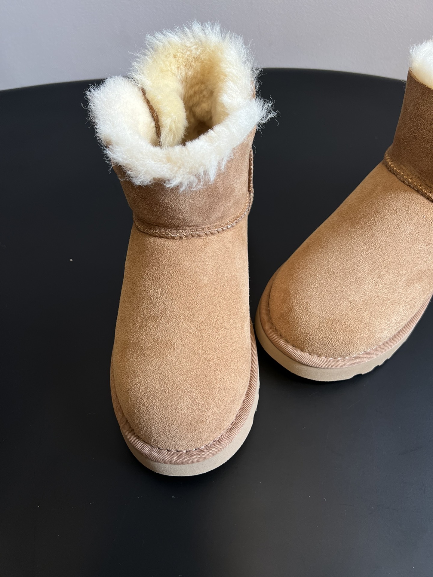 UG* 秋冬保暖圆扣logo短款雪地靴采用羊皮毛一体材质，鞋面是质感细腻的反绒皮，内里填充柔软的羊毛，既