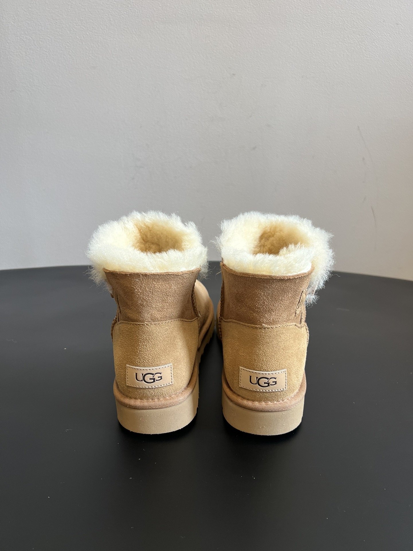 UG* 秋冬保暖圆扣logo短款雪地靴采用羊皮毛一体材质，鞋面是质感细腻的反绒皮，内里填充柔软的羊毛，既