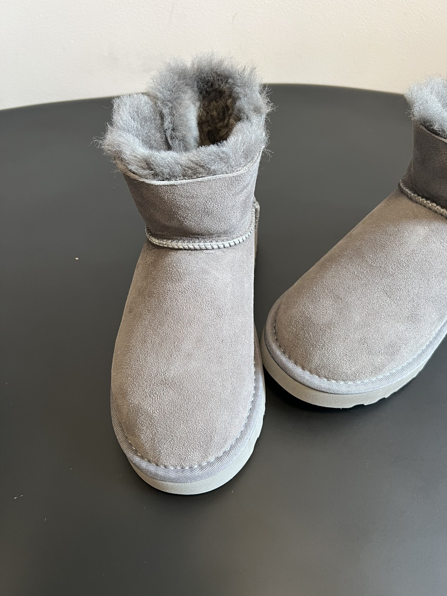 UG* 秋冬保暖圆扣logo短款雪地靴采用羊皮毛一体材质，鞋面是质感细腻的反绒皮，内里填充柔软的羊毛，既