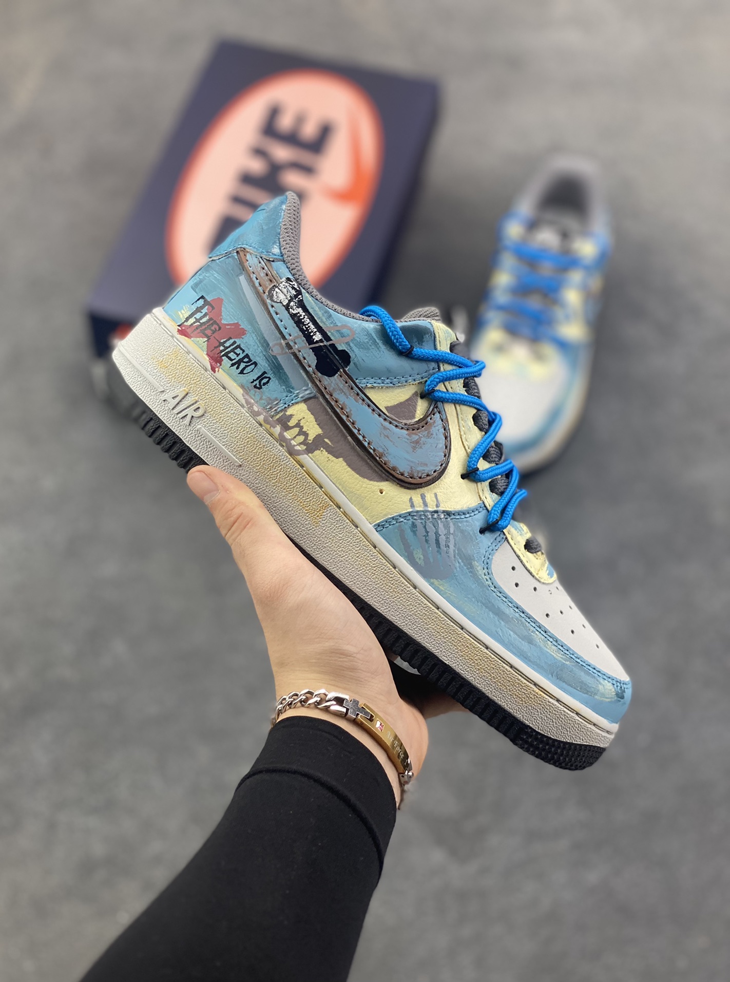 手绘涂鸦“雾蓝英雄”Nike Air Force 1 “Mist Blue Hero”空军一号定制板鞋 鞋身裹着一层雾感蓝灰的晕染，像清晨街景被薄雾浸软的色调，做旧肌理里藏着随性的泼墨痕迹，自带慵懒的复古滤镜；亮眼的蓝色绳状鞋带是点睛之笔，软乎乎的绳结打破了鞋身的朦胧感，添了几分街头的跳脱劲儿。鞋侧的“THE HERO”涂鸦最是灵魂——手写字体混着随性的线条，像某个少年在旧墙面上随手写下的英雄梦 货号：ZG0088-228 尺码：36 36.5 37.5 38 38.5 39 40 40.5 41 42 42.5 43 44 44.5 45-选品中心