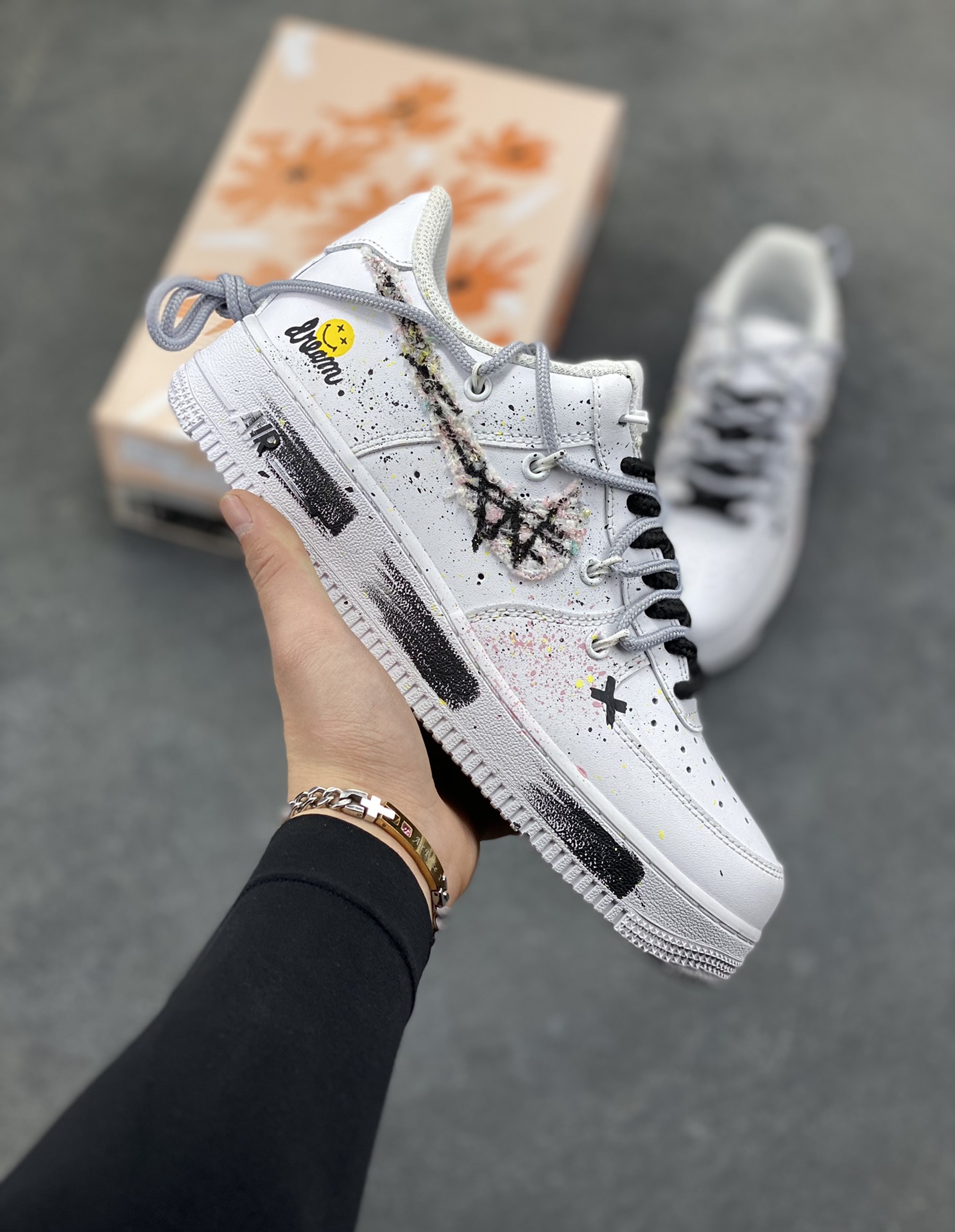 订制空军一号板鞋 该定制版球鞋选用原鞋款为Nike Air Force 1‘07空军一号，身铺满黑白泼墨+手绘纹理，混着细碎彩点，像随手挥洒的街头手稿；鞋侧贴了笑脸标+手写字样，再加上一块“毛边破缝”的拼接料，甜感里掺了点废土风的随性；连鞋带都用了黑白撞色，中底也加了黑线条点缀，细节里全是“不撞款”的小心思。 货号：DH1999-334 尺码： 36 36.5 37.5 38 38.5 39 40 40.5 41 42 42.5 43 44 44.5 45-选品中心