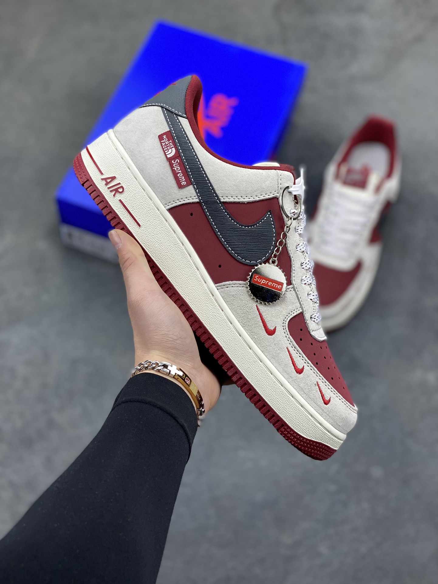 Nike Air Force 1 Low x Supreme x The North Face 三方联名酒红灰配色，直接把街头潮流与户外机能风焊死在鞋面上！酒红麂皮碰撞浅灰磨砂质感，鞋身多道迷你红勾打破常规，侧边Supreme×TNF织标强强联手，藏青Swoosh做旧处理更添复古韵味。白红中底刻字“Air”细节拉满，酒红外底踩出吸睛步调，挂饰吊坠更是把联名仪式感拉满。经典AF1鞋型加持，不管是搭配工装裤还是牛仔潮搭，都能轻松拿捏高阶街头感，这双SY1388-014绝对是潮人鞋柜里的收藏级狠货！-选品中心