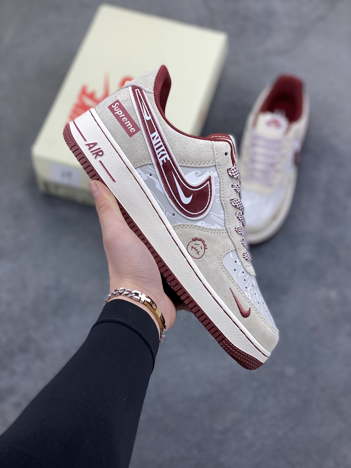 解构潮范，低帮新绎｜Nike Air Force 1 Low x Supreme联名款！当Nike Air Force 1 Low的经典街头底蕴碰撞Supreme的硬核潮牌基因，这双SS1979-012联名款成为街头潮流跨界的又一重磅之作，将复古板鞋的魅力与潮牌的个性表达融合到极致。 鞋身以浅米翻毛皮革为主调，酒红色饰条勾勒出利落的轮廓线条，材质的细腻质感与色彩的撞色搭配，瞬间拉满视觉层次。解构主义设计的双层Swoosh打破常规，酒红主Swoosh叠搭白色细勾，侧边印刻的“NIKE”与Supreme方块标识相互呼应，鞋舌处的编织鞋带、鞋身的涂鸦风暗纹，每一处细节都暗藏联名的巧思。鞋侧的小勾刺绣、中底的“Air”字样与酒红外底的组合，延续了Air Force 1 Low的经典轮廓，又为鞋款注入了Supreme标志性的潮酷灵魂。浅米中底搭配酒红外底，兼顾了复古脚感与潮流视觉，让这双联名款既能适配街头工装风穿搭，也能融入高街休闲造型。无论是潮牌爱好者的收藏清单，还是日常出街的吸睛选择，这双Nike Air Force 1 Low x Supreme都能以解构潮范的独特气质，让你轻松成为街头焦点。-选品中心