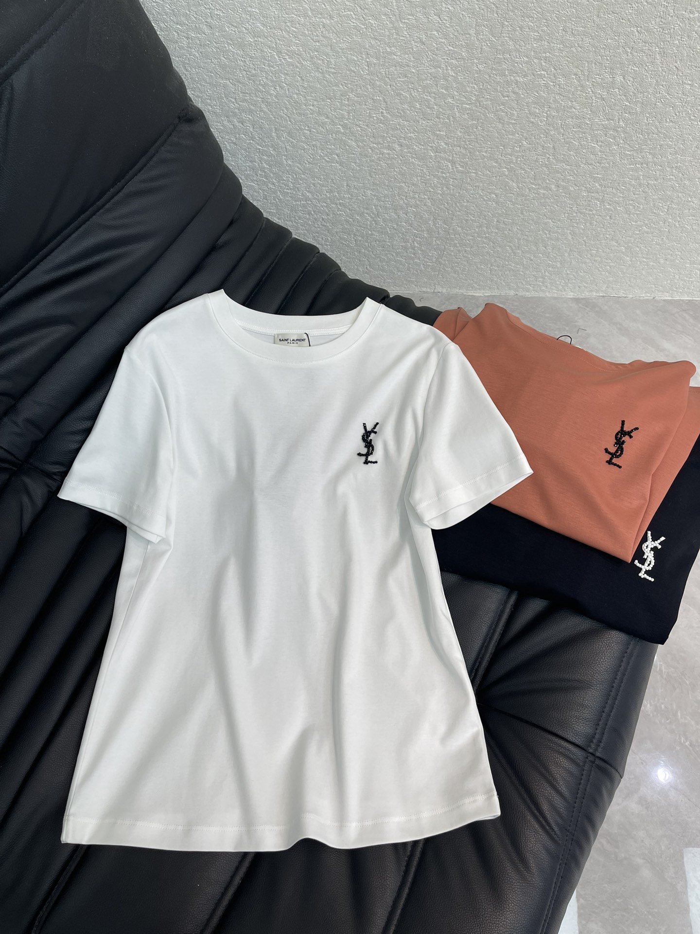 NO:696955,Saint lauren*26 new spring and summer YSL beaded letter logo short-sleeved T-shirt. Customized YB mercerized cotton material, breathable and comfortable, full of texture, regular short-sleeved T-shirt cut, this T-shirt has a simple and high-end feel welded to the body!  The letter logo on the chest is three-dimensional and eye-catching with beading technology. The soft and waxy fabric is skin-friendly and breathable. The basic round neck version is not flattering on the body shape. Whether worn alone to create a casual casual style, or layered with shirts and sweatshirts as inner wear, it is a versatile king that will never go out of style in the wardrobe. SML AA,, saint laurent, saint laurent, hoodie, sweatshirts, shirts, T-shirt, tees, t-shirt,19860909Saint lauren*26春夏新款Ysl钉珠字母徽标短袖T恤.定制YB丝光全棉材质,透气舒适,质感十足,常规短袖T恤裁剪,这款T恤把简约高级感焊在身上了！胸口的字母标识以钉珠工艺立体呈现低调又吸睛,软糯的面料亲肤又透气,基础圆领版型不挑身形,不管是单穿打造随性休闲风,还是叠穿衬衫、卫衣做内搭,都是衣橱里永不过时的百搭王.SML AA,,saint laurent,saint laurent,hoodie,sweatshirts,shirts,T-shirt,tees，t-shirt,,Women's clothing