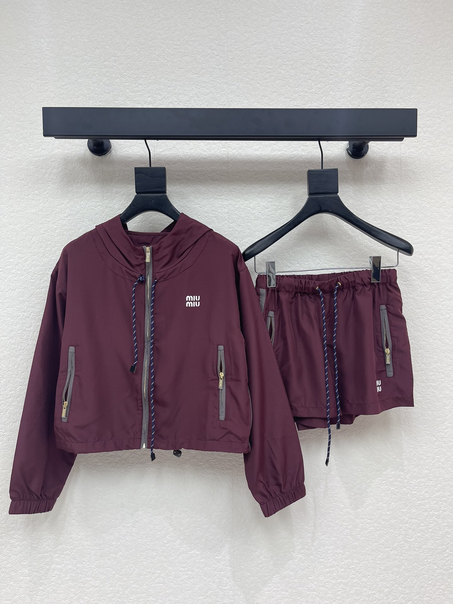 NO:715912,Jacket Shorts Miumi*26 Early Spring New Burgundy Hooded Micro Label Jacket Jacket + Shorts Set丨Exclusively developed by yb!  Top quality production!  The main color is retro and rich burgundy. The lightweight nylon fabric has a delicate luster and is both windproof and breathable. It is an excellent choice for the early spring season. The hooded jacket is cut with loose shoulders, with a drawstring design and a contrasting zipper, integrating exquisite details into the casual sports style; the shorts of the same series continue the jacket's style.  The design language, side zippers and drawstring waistband are both practical and stylish. The whole set does not need to be thought about, and it can easily create a relaxed and fashionable sweet and cool girly feel19860909外套 短裤Miumi*26早春新款酒红色连帽微标夹克外套+短裤套装丨独家yb开发！顶级高版出品！以复古浓郁的酒红色为主调,轻盈的尼龙面料自带细腻光泽感,兼具防风性与透气性,是早春换季的绝佳选择.连帽夹克采用宽松落肩剪裁,搭配抽绳设计与撞色包边拉链,在休闲运动风中融入精致细节；同系列短裤延续了夹克的设计语言,侧边拉链与抽绳腰头兼具实用性与造型感.整套搭配无需费心思考,轻松打造松弛又时髦的甜酷少女感,无论是单穿还是叠穿,都能成为早春街头的吸睛焦点.SML,,miumiu,shorts,jackets & coats,jackets & coats,hats,,Women's clothing