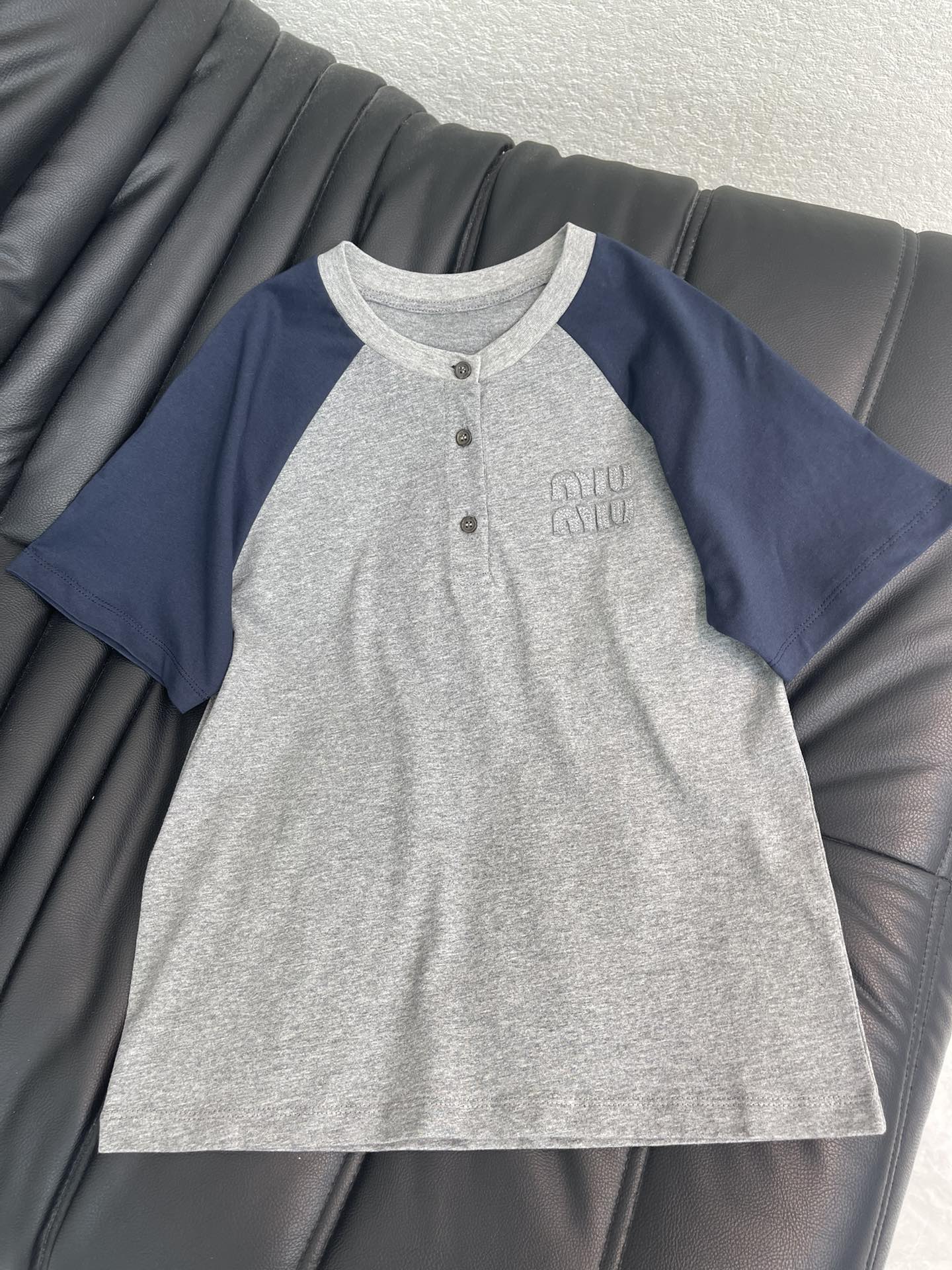 NO:716985,MiuMi*26 new color-blocked raglan short-sleeved T-shirt for spring and summer, gray + navy blue stitching, full of college style, soft cotton fabric, super comfortable to wear, a must-have for spring and summer. The button design on the neckline is full of details, and the brand embroidered logo on the chest is very recognizable. It can be easily worn in daily casual and street style. It goes well with jeans or short skirts. It is a popular item this season!  SML AA,,miumiu,skirts,jeans,T-shirt,tees,t-shirt,19860909MiuMi*26春夏新款拼色插肩短袖T恤,灰色+藏蓝拼接,学院风满满,柔软棉质面料,穿着超舒适,春夏必备.领口纽扣设计,细节感拉满,胸前品牌刺绣徽标超有辨识度,日常休闲、街头风都能轻松驾驭,搭牛仔裤或短裙都很出彩,是本季热门单品！SML AA,,miumiu,skirts,jeans,T-shirt,tees，t-shirt,,Women's clothing