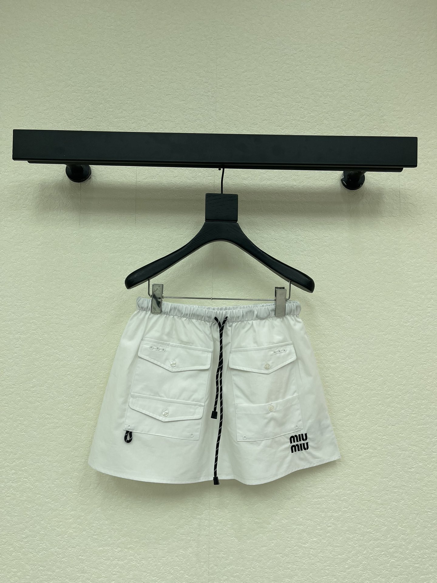 NO:731340,Miumi*26 early spring new letter logo pocket mini skirt丨exclusively developed by yb!  Top quality production!  Made of crisp cotton poplin, it creates an A-line silhouette that has both a workwear feel and a girly feel. The drawstring design at the waist can be freely adjusted to fit different waistlines; the multi-pocket details echo the mini letter logo on the side, injecting retro vitality into the pure white skirt. Whether paired with a velvet sweater to create a sweet and cool college style, or combined with a short vest for a hot girl look, it can be the finishing touch of an early spring look, easily balancing relaxation and sophistication. SML  AA,,miumiu,hoodie,sweatshirts,skirts,19860909Miumi*26早春新款字母徽标口袋迷你半身裙丨独家yb开发！顶级高版出品！以挺括的棉质府绸为面料,打造出兼具工装感与少女感的A字廓形.腰部的抽绳设计可自由调节松紧,适配不同腰围；多口袋细节与侧边的迷你字母徽标相呼应,为纯白裙身注入复古活力.无论是搭配丝绒卫衣打造甜酷学院风,还是与短款背心组合出辣妹感,它都能成为早春造型的点睛之笔,轻松平衡松弛感与精致感.SML AA,,miumiu,hoodie,sweatshirts,skirts,,Women's clothing