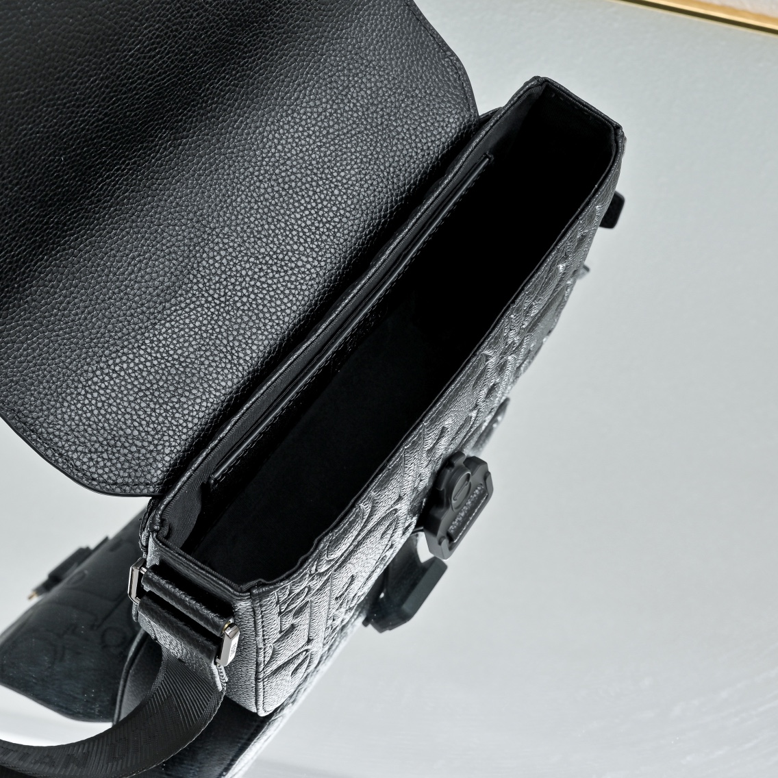 马鞍插扣压花信使包精巧时尚。采用米色和黑色 Oblique 印花面料精心制作，饰以黑色粒面牛皮革翻盖和“