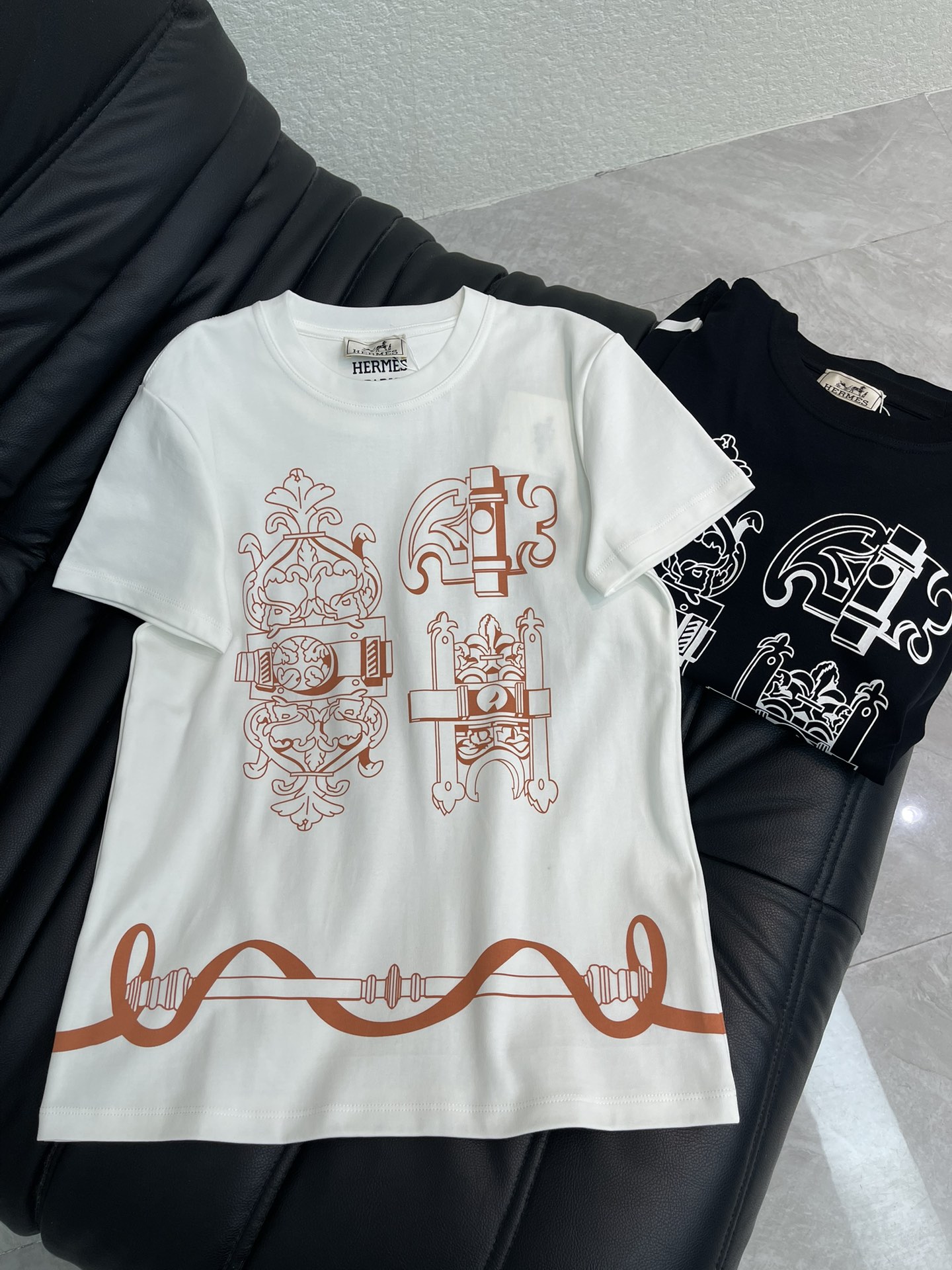 NO:734605,Hermes*26 new spring and summer short-sleeved T-shirt with chain positioning print. This T-shirt is presented in black and white, using a printing design that combines retro machinery and Baroque style. The lines are complex and artistic, and the overall style combines street fashion and artistic flavor. The white version is matched with brown-red lines, while the black version is outlined with white lines. The visual contrast is strong and suitable for wear enthusiasts who pursue individual expression. Whether it is for daily outings or art exhibitions, it can easily become the focus!  SML,,hermes,T-shirt,tees,t-shirt,19860909Hermes*26春夏新款器具链条定位印花短袖T恤.这款T恤以黑白双色呈现,采用复古机械与巴洛克风格融合的印花设计,线条繁复而富有艺术感,整体风格兼具街头潮流与艺术气息.白色款搭配棕红色线条,黑色款则以白色线条勾勒,视觉对比强烈,适合追求个性表达的穿搭爱好者.无论是日常出街还是艺术展览穿搭,都能轻松成为焦点！SML,,hermes,T-shirt,tees，t-shirt,,Women's clothing
