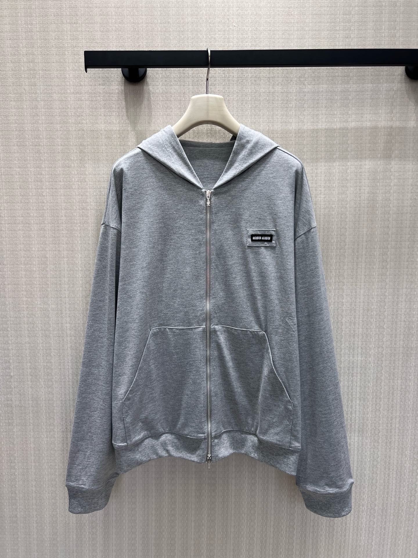 NO:910540,26 spring and summer new products  Miu** hemp gray hooded zipper sweatshirt interprets low-key casual aesthetics. The soft floral gray fabric is soft and smooth, delicate and skin-friendly with a matte high-end texture. The full zipper closure is paired with a classic kangaroo pocket, and the dropped shoulders and wide sleeves are tailored to relax and accommodate the body shape, without deliberately modifying it.  Lazy atmosphere. The mini woven label on the left chest is engraved with the brand logo in a low-key manner, abandoning the exaggerated design, and using minimalist lines to outline the Italian girly style. Wearing alone is casual and refreshing, suitable for wearing with a shirt or a coat, making it easy to wear in daily wear without revealing the exquisite elegance. Ready in stock sml  Actual detailed pictures,,miumiu,hoodie,sweatshirts,shirts,hats,1986090926春夏新品 Miu**麻灰连帽拉链卫衣,诠释低调千金休闲美学.柔和花灰面料软糯垂顺,细腻亲肤自带哑光高级质感.全拉链开合搭配经典袋鼠兜,落肩阔袖剪裁松弛包容身形,不刻意修饰却自带慵懒氛围.左胸迷你织标低调镌刻品牌标识,摒弃浮夸设计,用极简线条勾勒意式少女格调.单穿随性清爽,内搭衬衫、外搭大衣皆适配,日常穿搭轻松拿捏不露声色的精致贵气.现货smL 实拍细节图,,miumiu,hoodie,sweatshirts,shirts,hats,,Women's clothing