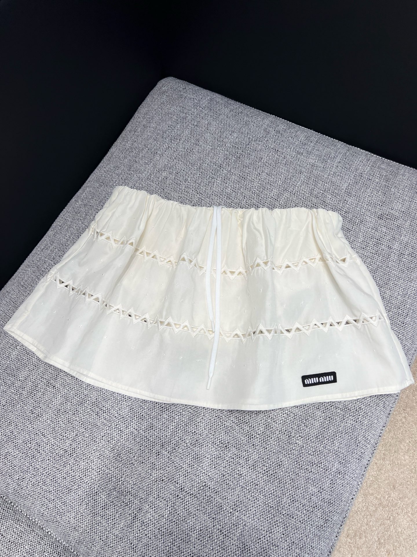 NO:912094,26 spring and summer new products  Miu** milk white hollow one-shoulder short top, replica of Italian retro sweet temperament. Soft waxy textured cotton material with soft matte texture, elastic one-line collar with puff short sleeves, gently revealing the shoulder and neck lines. The triangular hollow cut all over the body is transparent and light, with exquisite layers and not exaggerated.  The front mini woven label is engraved with the brand logo in a low-key manner, neutralizing the sweetness and adding light luxury. The short waisted version raises the waistline and is suitable for matching with the hollow skirt of the same series. It is suitable for daily appointments and short trips. It is a gentle and smart gold-style top. In stock 36/38/40  Actual detailed pictures,,miumiu,skirts,T-shirt,1986090926春夏新品 Miu**奶白镂空一字肩短上衣,复刻意式复古清甜气质.软糯肌理棉料自带柔和雾面质感,松紧一字领搭配泡泡短袖,温柔展露肩颈线条.周身错落三角镂空剪裁通透轻盈,层次精致不浮夸,胸前mini织标低调镌刻品牌标识,中和甜腻增添轻奢底蕴.短款收腰版型拉高腰线,适配同系列镂空半裙成套穿搭,日常约会、短途出游皆适配,温柔又灵动的千金风上衣.现货36/38/40 实拍细节图,,miumiu,skirts,T-shirt,,Women's clothing