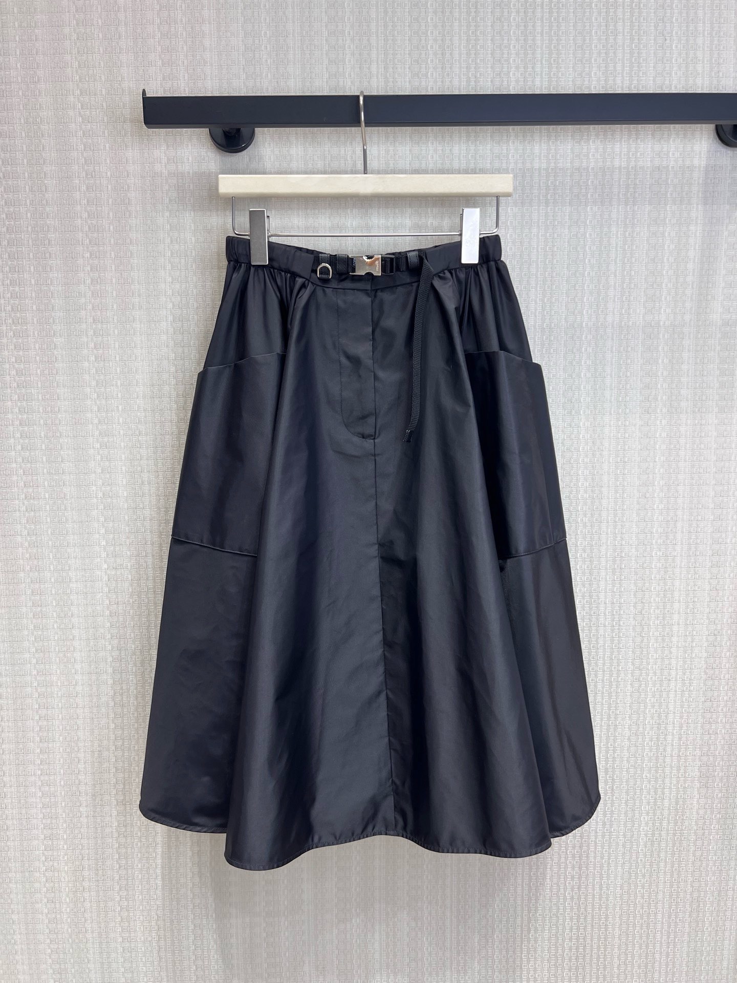 NO:944610,26 spring and summer new product Pra**'s iconic regenerated nylon fabric has a matte high-end texture, is stiff and anti-wrinkle, and has a stylish drape. The soft pleats create a three-dimensional umbrella shape, with functional belt and metal buckle details, which combines elegant feminine lines with practical workwear attributes. The large pockets on both sides are designed to take into account both style and practicality. The mid-length A-line version perfectly modifies the waist and hip lines, hides the flesh and makes you look slimmer, and is suitable for many styles. Available now smL  Real shot details,,prada,1986090926春夏新品 Pra**标志性再生尼龙面料,自带哑光高级质感,挺括抗皱,垂坠有型. 柔和褶皱打造立体伞状廓形,搭配机能风腰带与金属扣细节, 兼具优雅女性化线条与实用工装属性,两侧大口袋设计兼顾造型与实用性, 中长A字版型完美修饰腰臀线条,藏肉显瘦,适配多风格搭配.现货出售smL 实拍细节图,,prada,,Women's clothing
