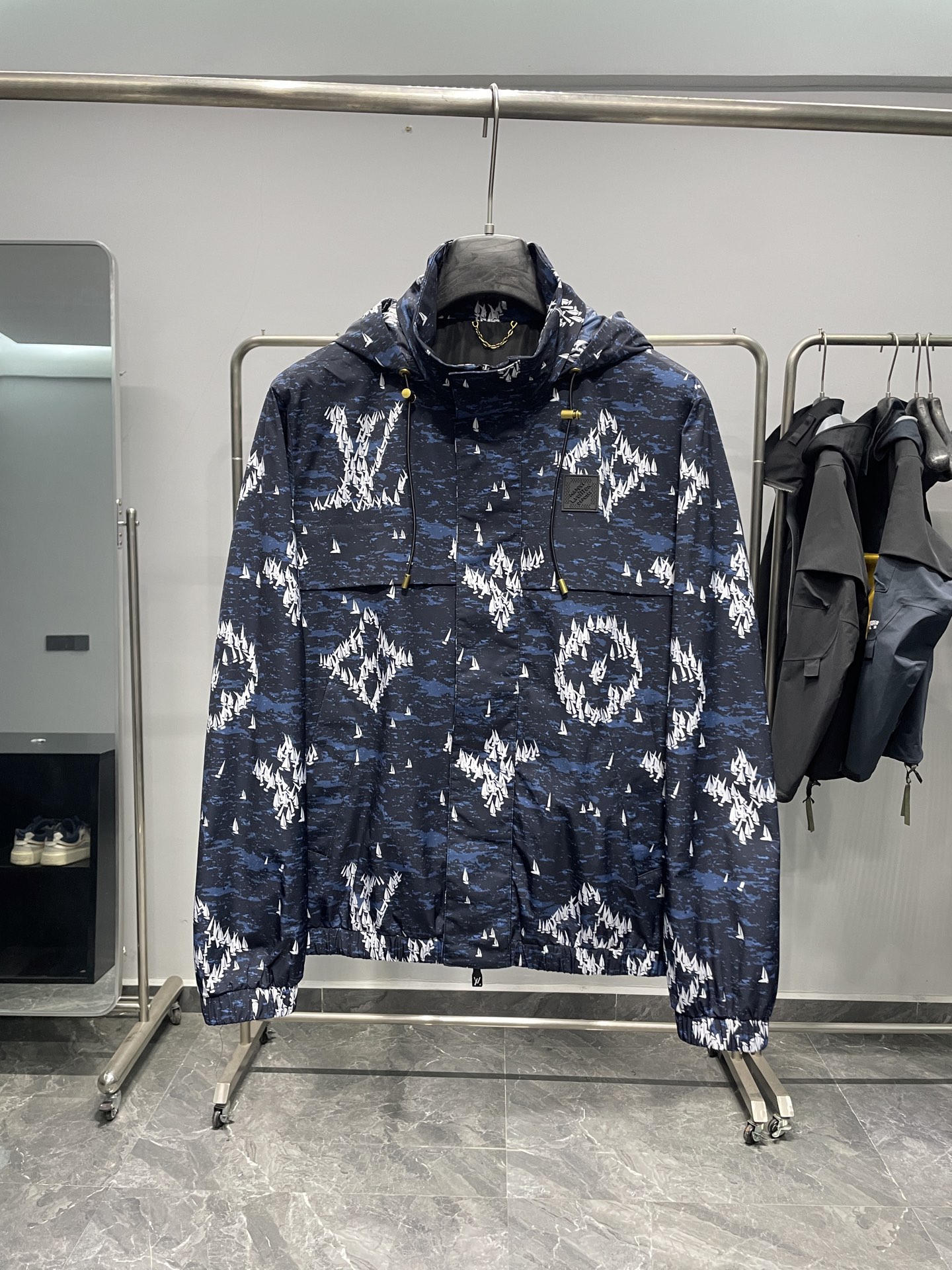 NO:518779,1V25FW autumn new dark blue sailboat printed nylon hooded windbreaker jacket!  It is made of dark blue as the background and is covered with white sailboat printing patterns, which combines fashion and uniqueness. The hooded design is casual and has certain wind and rainproof functions, and is suitable for wearing in various occasions. The hat is equipped with a drawstring, and the metal pendant at both ends of the drawstring is engraved with logos to increase brand recognition. There is a black rubber logo on the left chest, with brand letter information imprinted on it, which is low-key and highlights the brand identity. The opening and closing of the clothes is a combination of zippers and snaps to increase the firmness of the closure. The zipper head is designed with a simple design, and there are also brand-related marks on the snaps. There is a larger pocket on the front to facilitate the placement of small items!  The cuffs and hem are elastic, which can effectively block the cold wind from entering, and are comfortable to wear and fit the body. The inner part is black, the material is smooth, and the skin feels comfortable when worn. In the inner part, there is also a gold chain decoration. The main material of this windbreaker jacket is made of nylon, which is wear-resistant and windproof. It is not easy to pill or damage when worn. When it comes to light wind, it can also play a certain barrier role to keep the body dry. Dark blue Size 48-56 Size reference Size 48: Shoulder width 47 bust 110 sleeve length 64 clothes 66 Size 50: Shoulder width 48 bust 114 sleeve length 65 clothes 67 Size 52: Shoulder width 49 bust 118 sleeve length 66 Size 68 Size 54: Shoulder width 50 bust 122 sleeve length 67 Size 69 Size 56: Shoulder width 51 bust 126 sleeve length 68 Size 70,, jackets &  coats, hats, alexander wang198609091V25FW秋季新款深蓝色帆船印花尼龙连帽风衣外套！以深蓝色为底色,布满白色帆船印花图案,兼具时尚感与独特性. 连帽设计,休闲且具有一定的防风防雨功能,适合多种场合穿着.帽子配有抽绳,抽绳两端的金属坠饰上刻有logo字样,增添品牌辨识度.左胸前位置设有一块黑色橡胶标识牌,上面压印着品牌字母信息,低调又彰显品牌身份.衣服开合处采用拉链与按扣结合的方式,增加闭合的牢固性,拉链头设计简洁 ,按扣上也有品牌相关印记. 正面设有较大的口袋,方便放置随身小物品！袖口和下摆处采用松紧设计,能有效阻挡寒风进入,穿着舒适且贴合身形.内里为黑色,材质顺滑,穿着时皮肤触感舒适.在内里部分位置,还设有金色链条装饰 这款风衣外套主料采用锦纶,耐磨又防风,日常穿不容易起球、破损,遇到小风天气,也能起到一定阻隔作用,保持身体干爽. 颜色深蓝色 尺码48-56 尺寸参考 48码:肩宽47胸围110袖长64衣长66 50码:肩宽48胸围114袖长65衣长67 52码:肩宽49胸围118袖长66衣长68 54码:肩宽50胸围122袖长67衣长69 56码:肩宽51胸围126袖长68衣长70,,jackets & coats,hats,alexander wang,Men's clothing