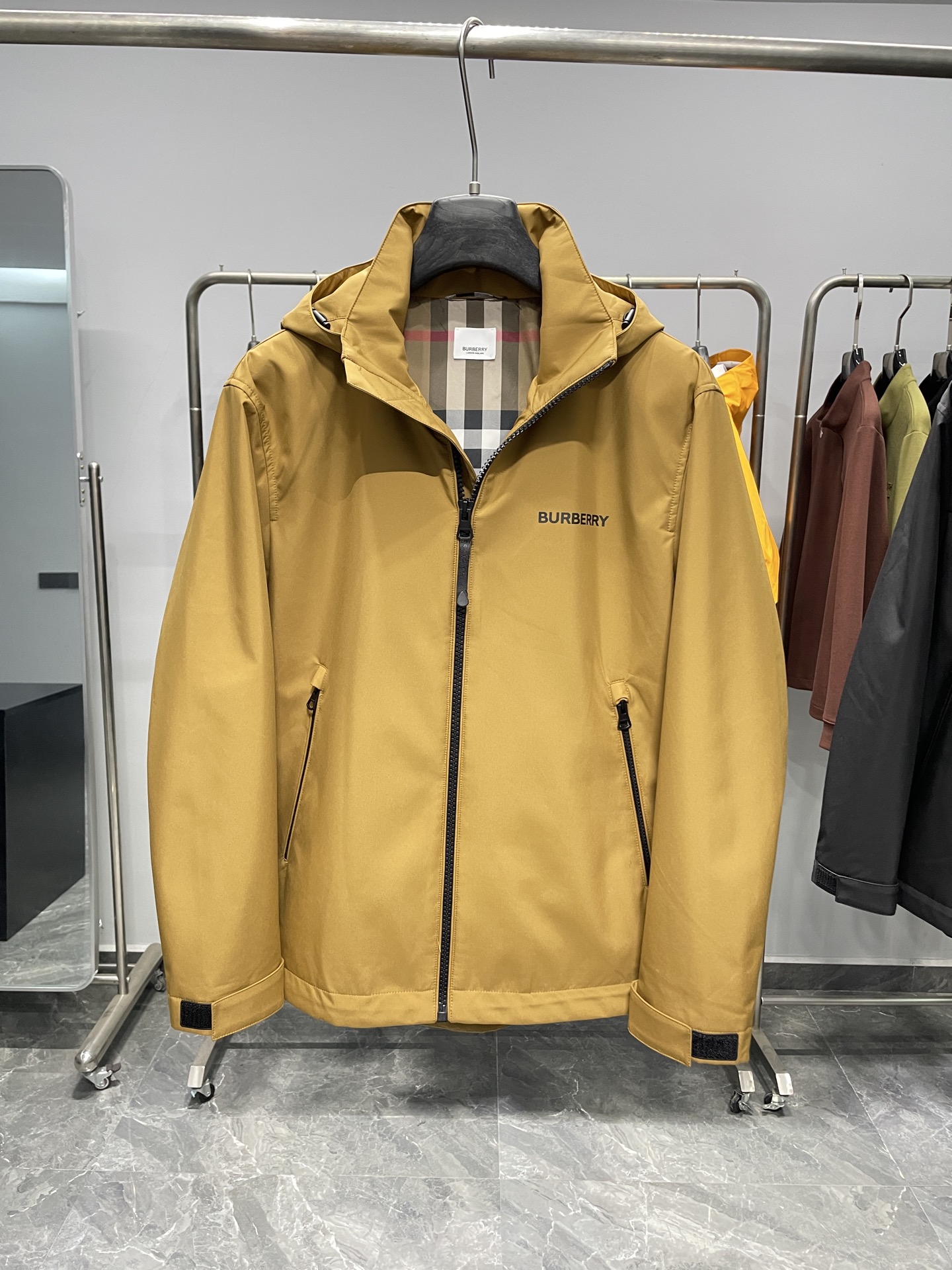 DBU6606P490～BUR25FW秋冬新品男女同款户外防风连帽软壳棉衣外套冲锋衣!整体版型较为宽松 ，穿着起来舒适自在，同时方便内搭不同厚度的衣物，适应多种场合和温度环境。
连帽设计，增添实用性和时尚感，能够在风雨天气为头部提供防护。
在胸前位置，有明显BUR品牌标识，黑色外套上是白色字体，黄色外套上是深色字体，增强了品牌辨识度！拉开拉链后，可以看到经典的格纹内衬，彰显品牌特色与高端质感。
外套正面采用品牌定制拉链，拉链头上刻有logo钢印，顺滑耐用，保证开合顺畅，同时拉链顶端设有防护装置，防止夹到皮肤或衣物 。两侧设有拉链口袋，可以安全存放随身物品，防止物品掉落，拉链设计也能在一定程度上防水。帽子带有调节装置，抽绳和调节扣的设计，可以根据需求调整帽子的松紧，更好地贴合头部，增强防风效果 。袖口处配备魔术贴调节装置，可以自由调整袖口的松紧度，既能防止冷风灌入，又能适应不同手腕粗细 。
外套外部主要面料为100%聚酯纤维，这种材质具有良好的防风、防水和耐磨性，适合户外穿着。内层为100%棉，亲肤舒适，能够提升穿着时的体感舒适度，避免皮肤与外层聚酯纤维直接接触可能产生的不适！

颜色：黄色、黑色
尺码：48-56
尺寸参考：
48码:肩宽48胸围112袖长60衣长70
50码:肩宽49胸围116袖长61衣长71
52码:肩宽50胸围120袖长62衣长72
54码:肩宽51胸围124袖长63衣长73
56码:肩宽52胸围128袖长64衣长74